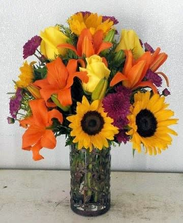 Bouquet of sunflowers, orange lilies, and purple flowers in a glass vase
