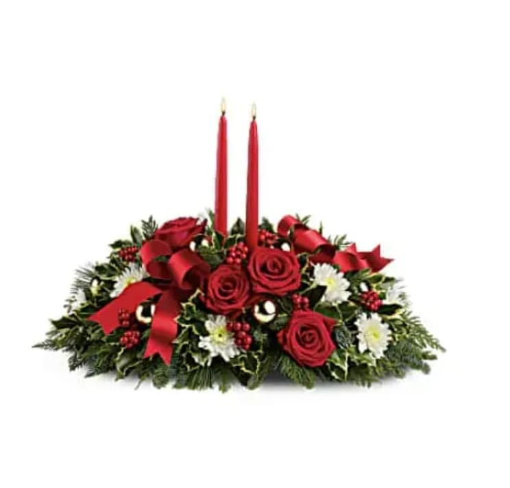 Holiday Shimmer Centerpiece - Make the season bright - and their table a delight - with the glowing tapers, radiant red roses and fresh Christmas greens of this stunning seasonal centerpiece. This stunning centerpiece features red roses, white cushion spray chrysanthemums, variegated holly, noble fir, flat cedar, white pine, red berries, gold ornament balls, red ribbon, and red taper candles. Orientation: All-Around