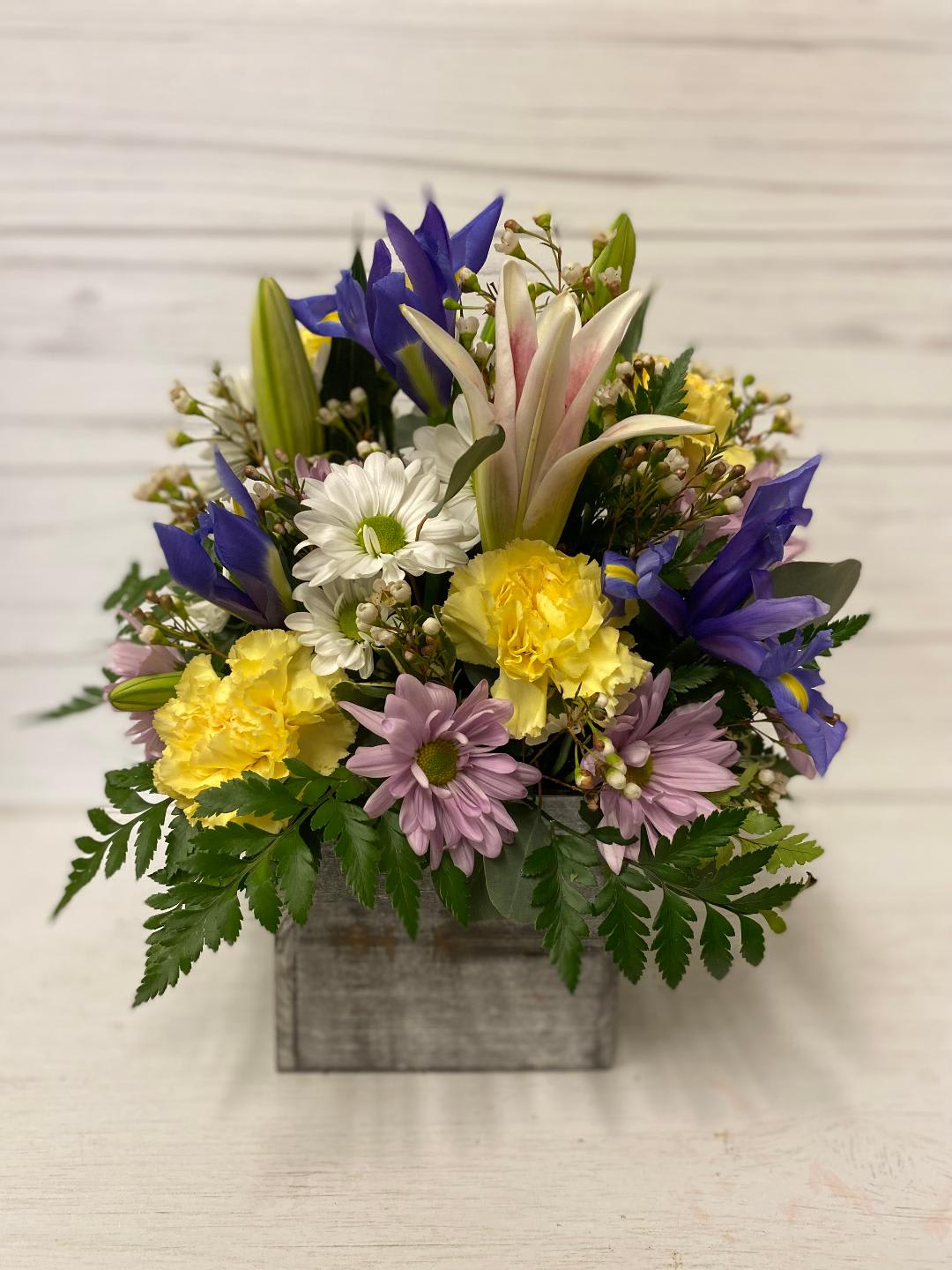 Mixed bouquet in a gray wooden box with blue, yellow, white, and lavender flowers