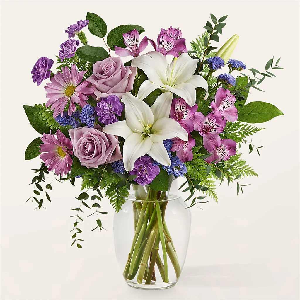 Lavender and white bouquet with lilies, roses, daisies, and alstroemeria in a clear glass vase.