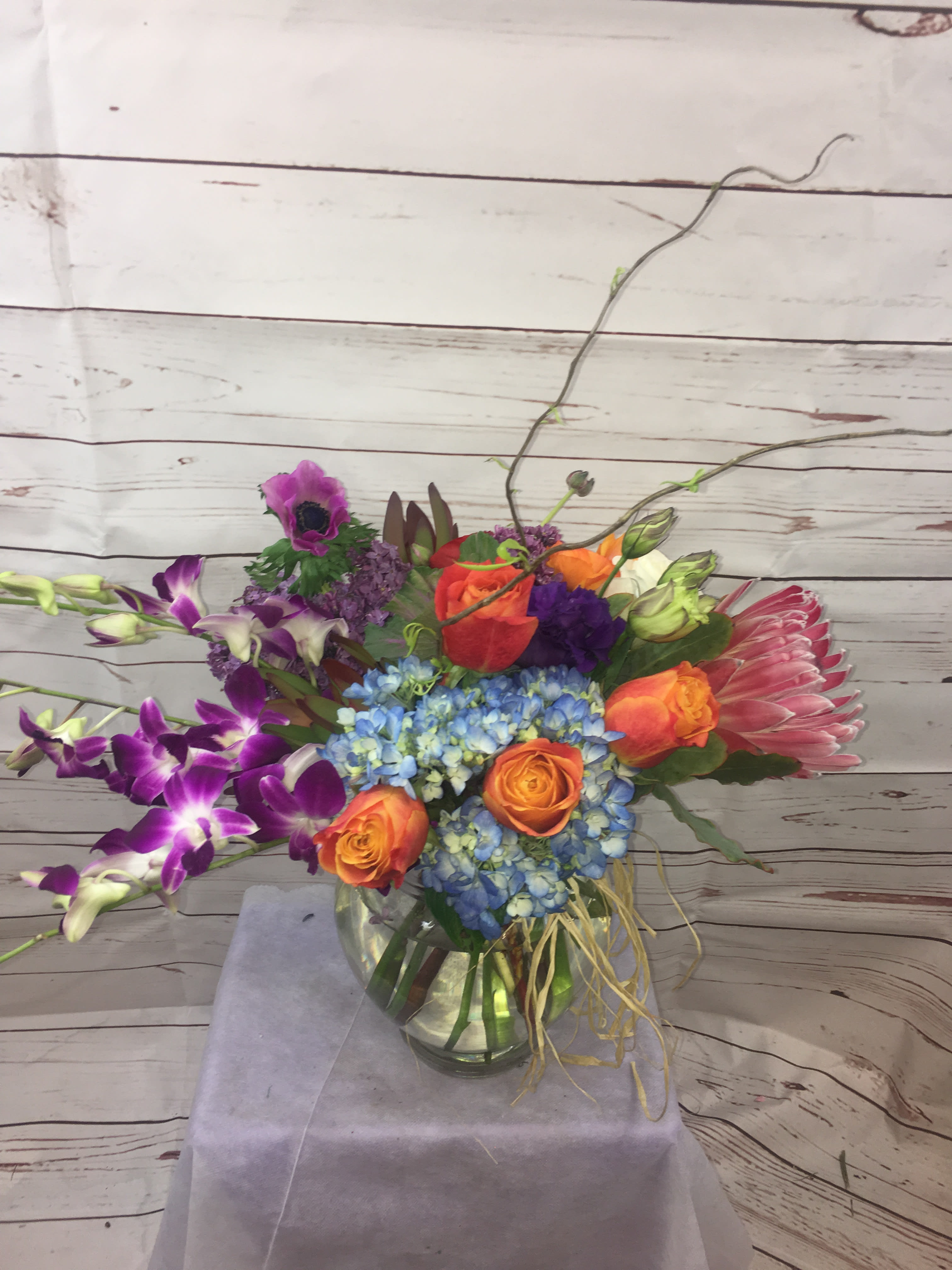 Colorful mixed bouquet in a glass vase with orange roses and blue hydrangea