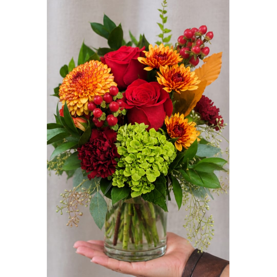 Bouquet of red roses, orange mums, and green hydrangea in a glass vase