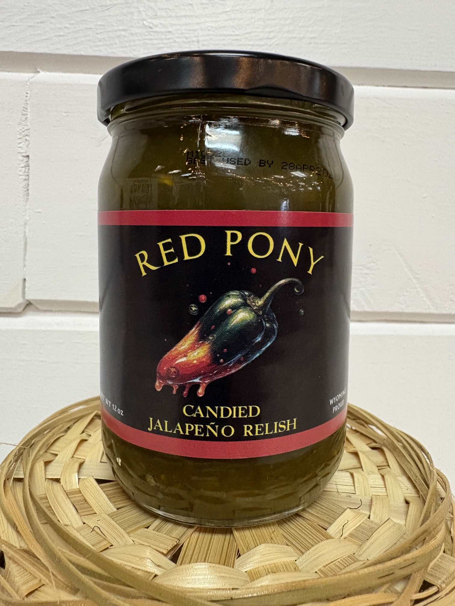 Jar of candied jalapeño relish with a black lid on a woven tray