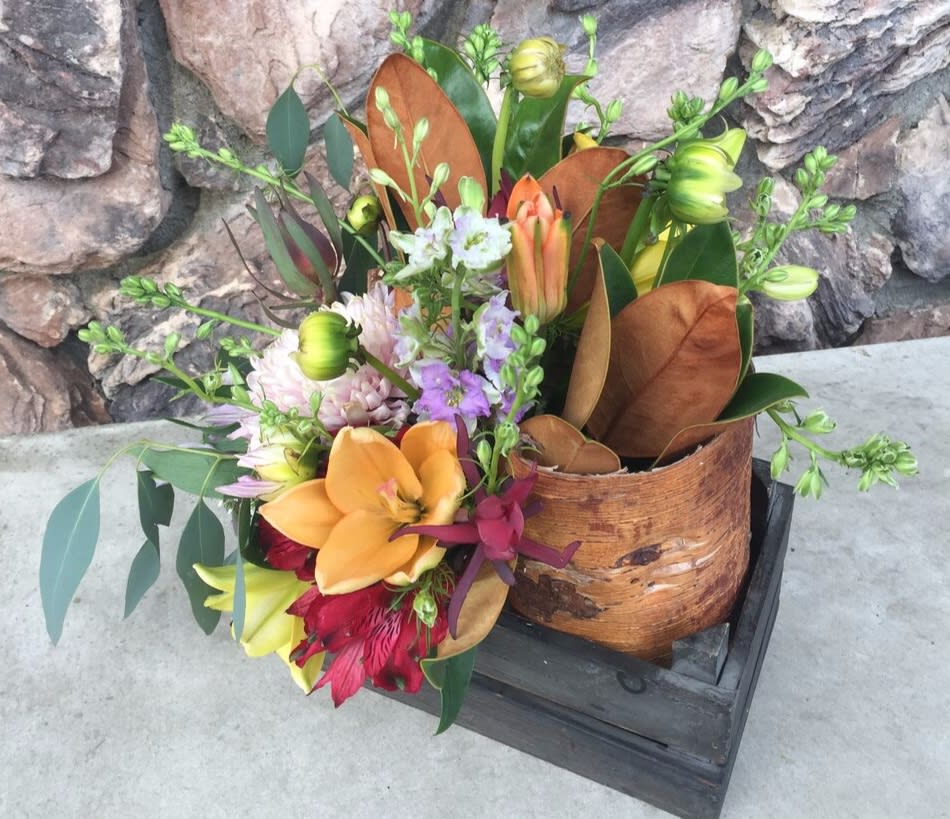 Mixed bouquet with orange lilies and purple flowers in a wooden container