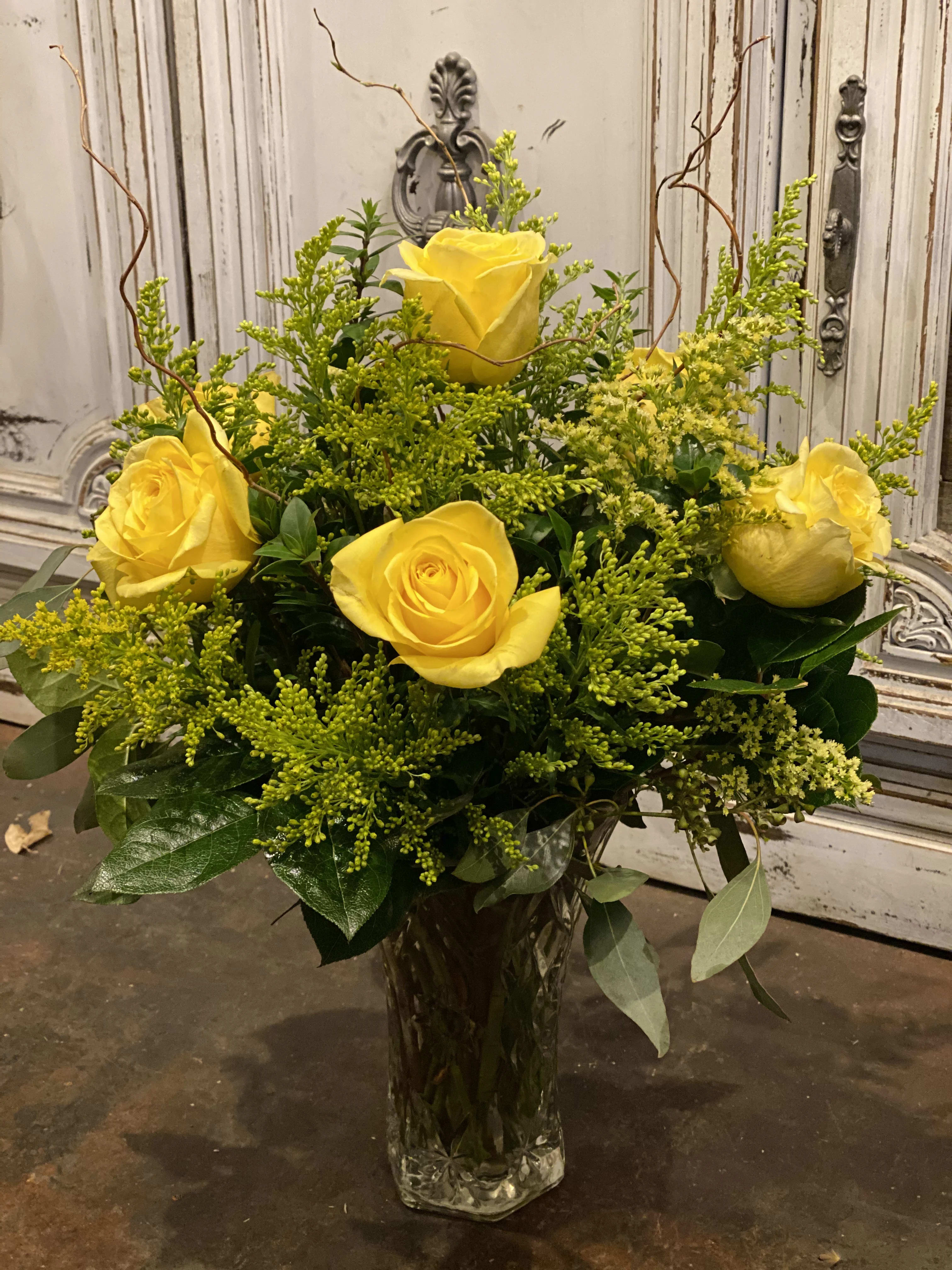 Yellow roses arranged in a clear glass vase with airy green filler