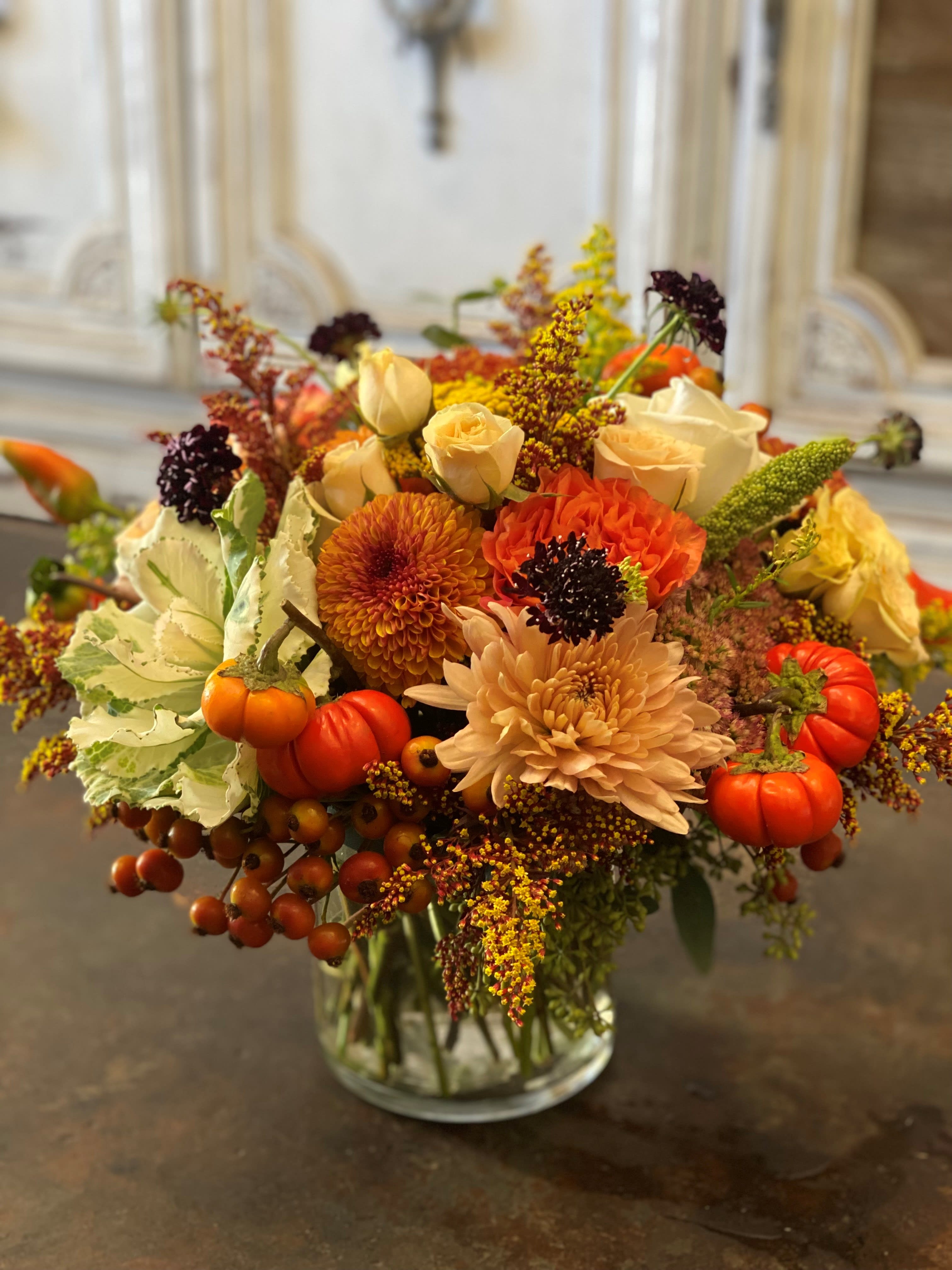 Autumn bouquet of orange and cream flowers in a glass vase with small pumpkins