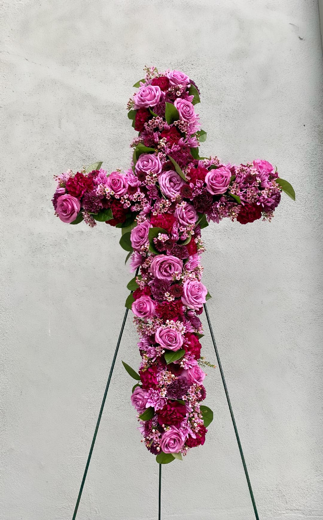 Standing floral cross of pink and burgundy blooms on a metal easel.