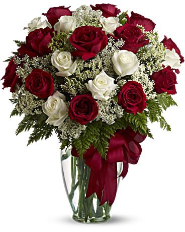 Arrangement of red and white roses in a clear glass vase with a red ribbon bow.