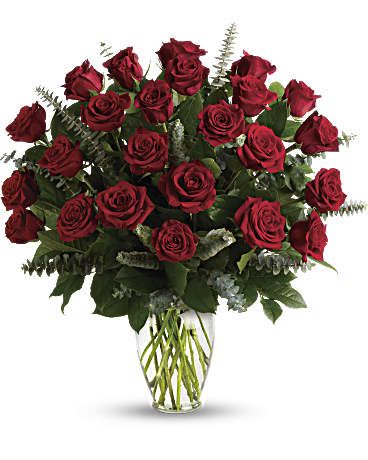 Large arrangement of dark red roses with eucalyptus in a clear glass vase.
