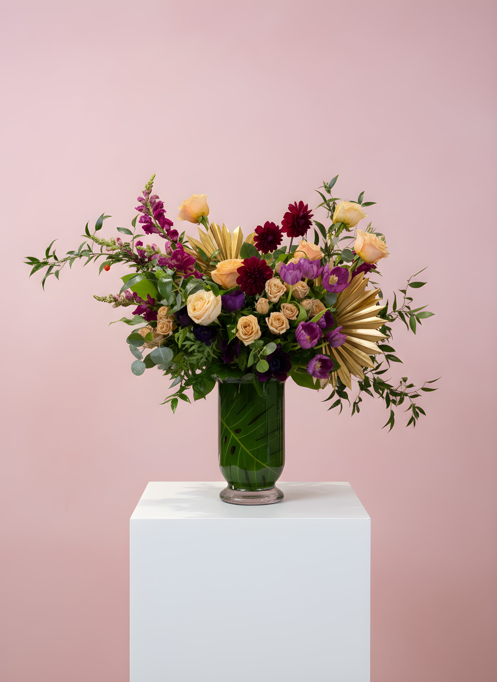 Tall peach, burgundy, and purple flower arrangement with gold accents in a green-filled glass vase.