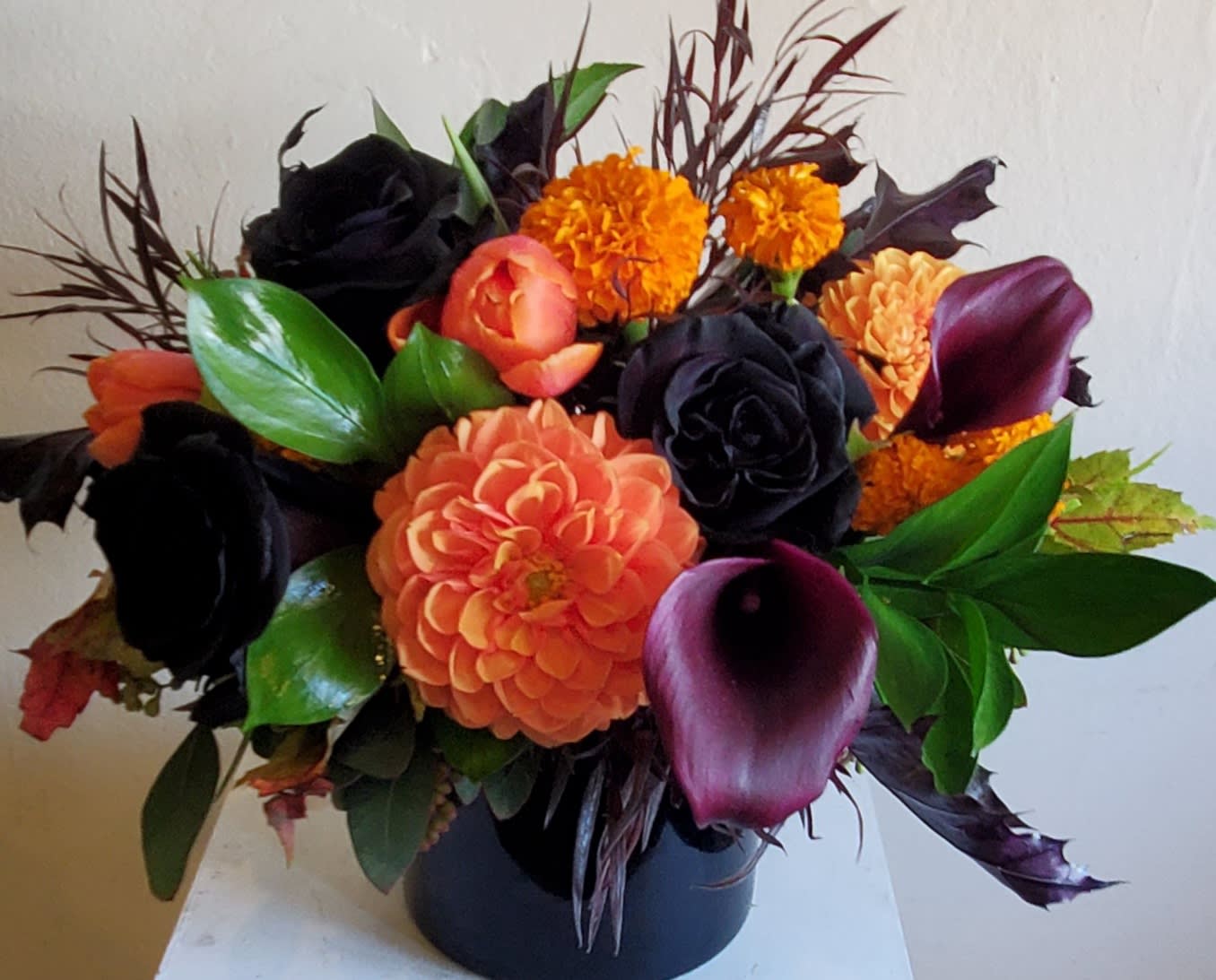 Orange and dark floral arrangement in a black vase with calla lilies and roses