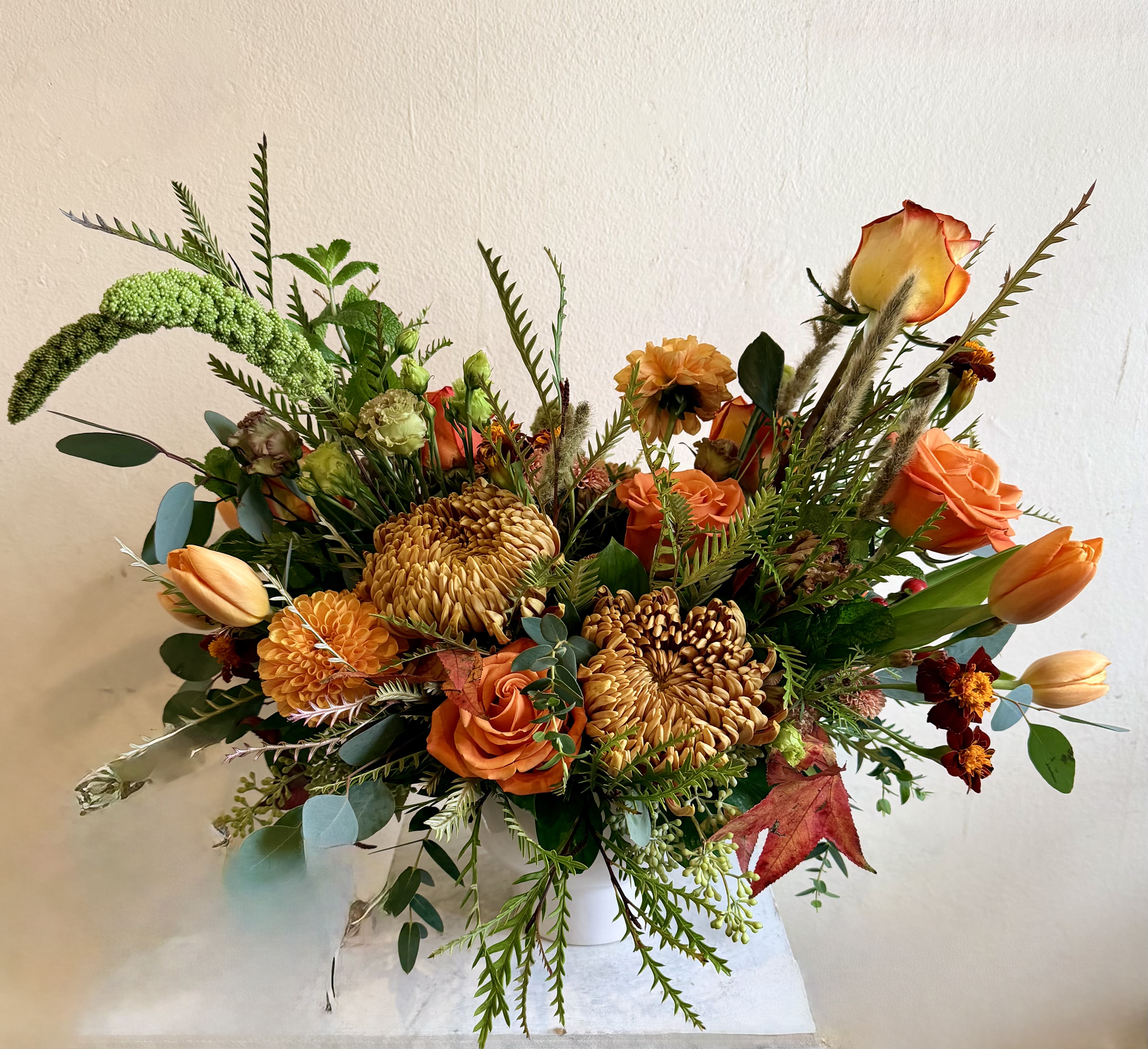 Orange and gold mixed bouquet in a white vase