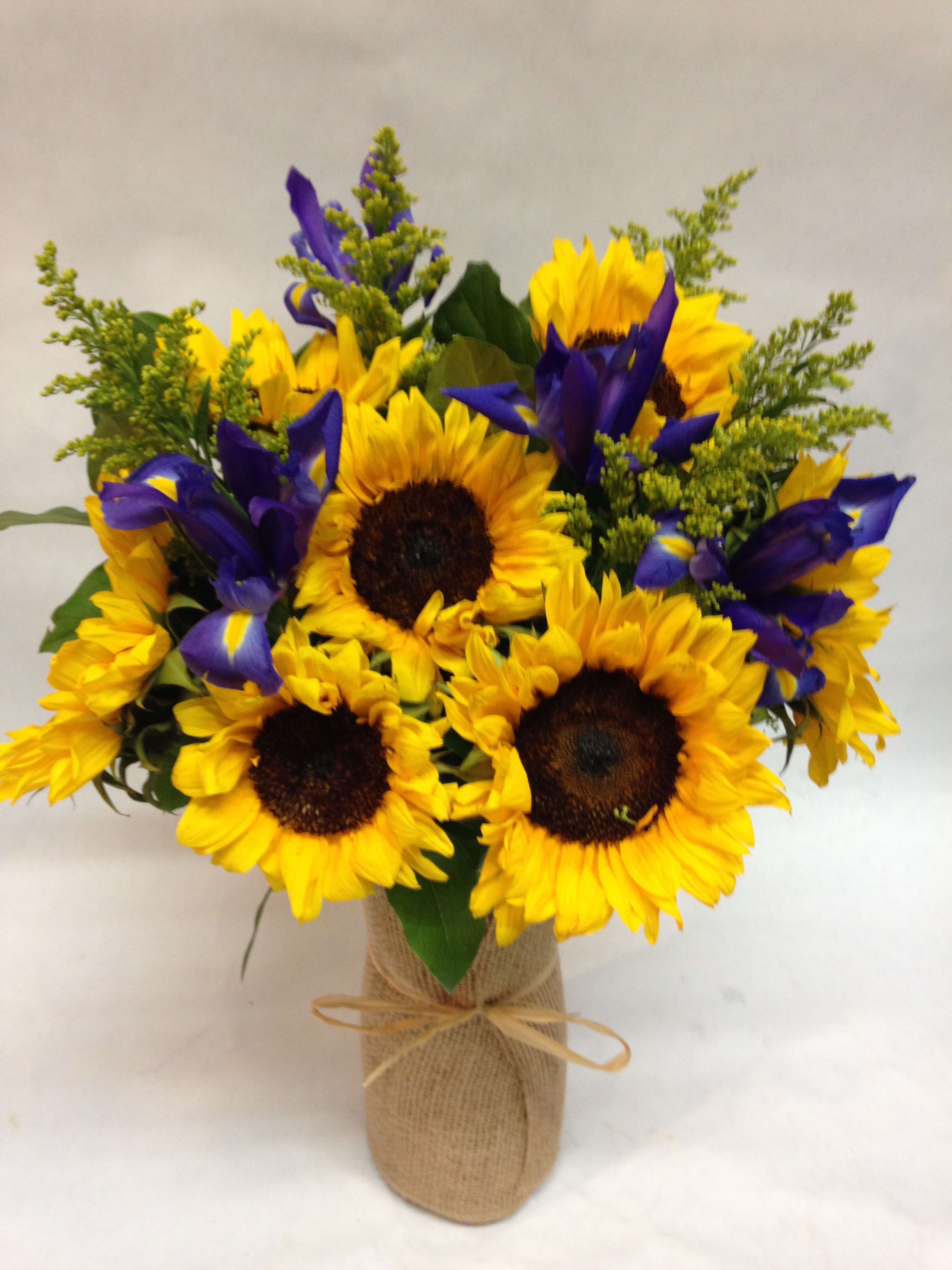 Bouquet of yellow sunflowers and purple irises in a burlap-wrapped vase