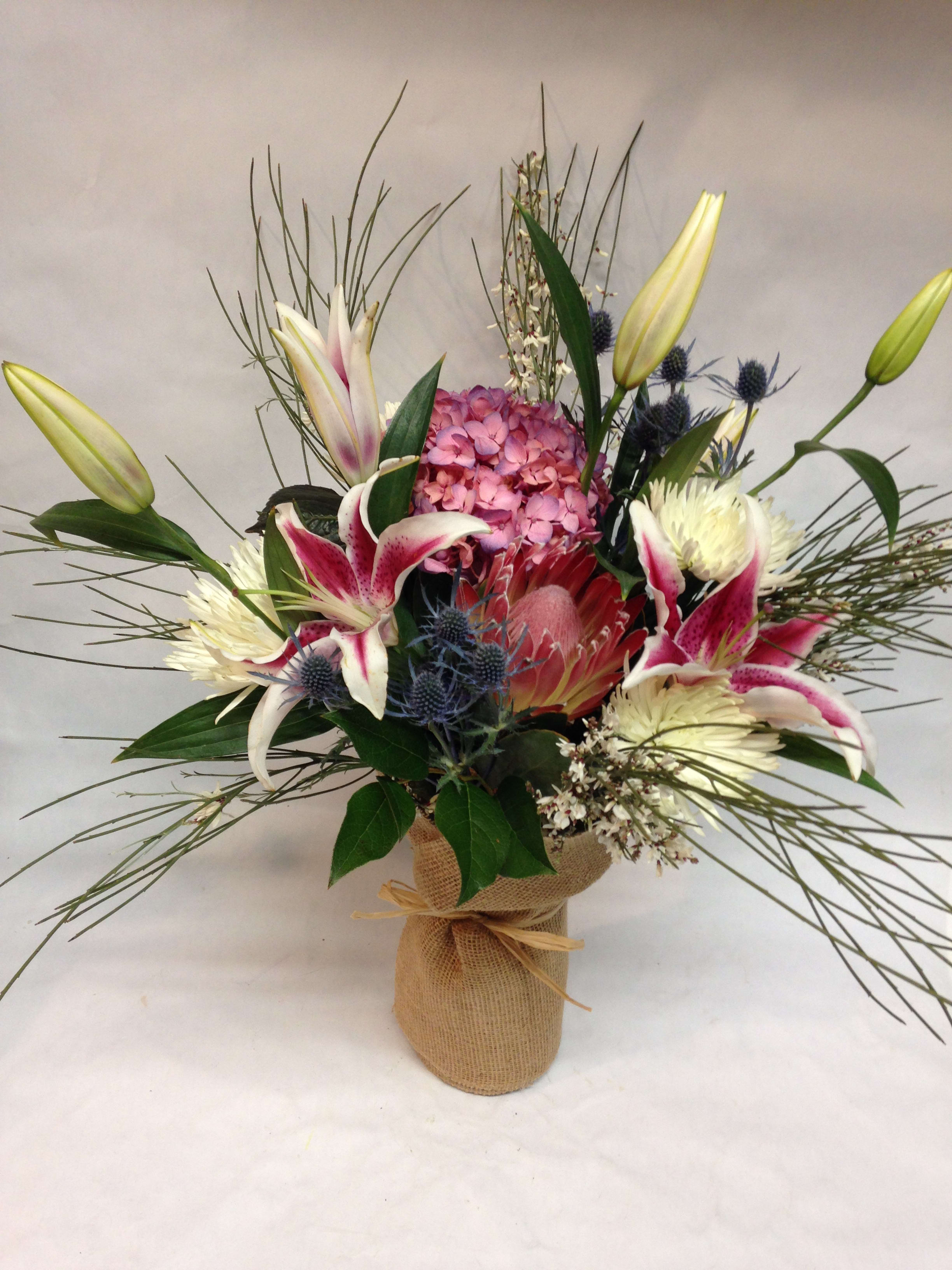 Mixed bouquet with lilies, hydrangea, and protea in a burlap-wrapped vase