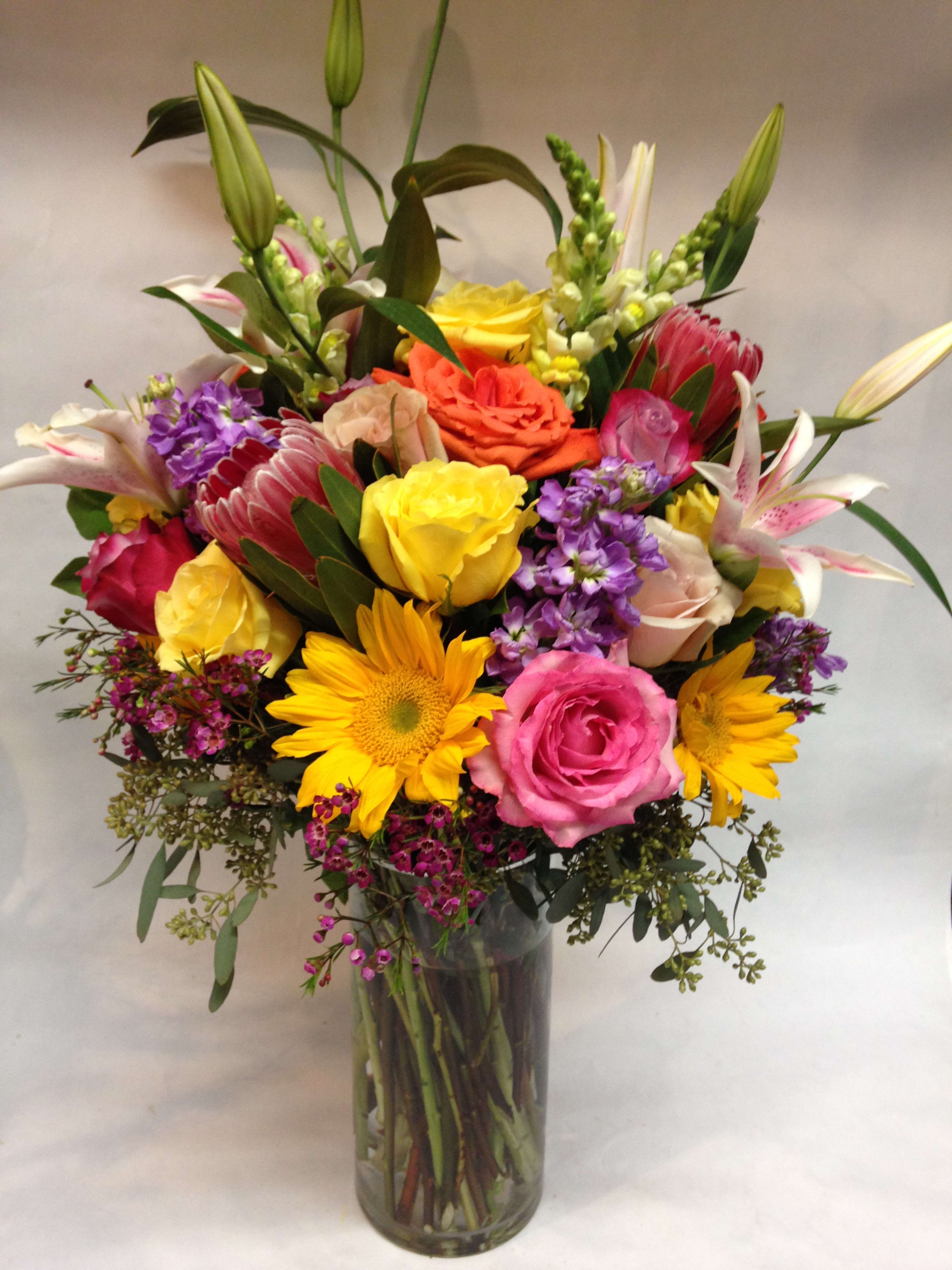 Mixed bouquet in a glass vase with roses, lilies, and sunflowers