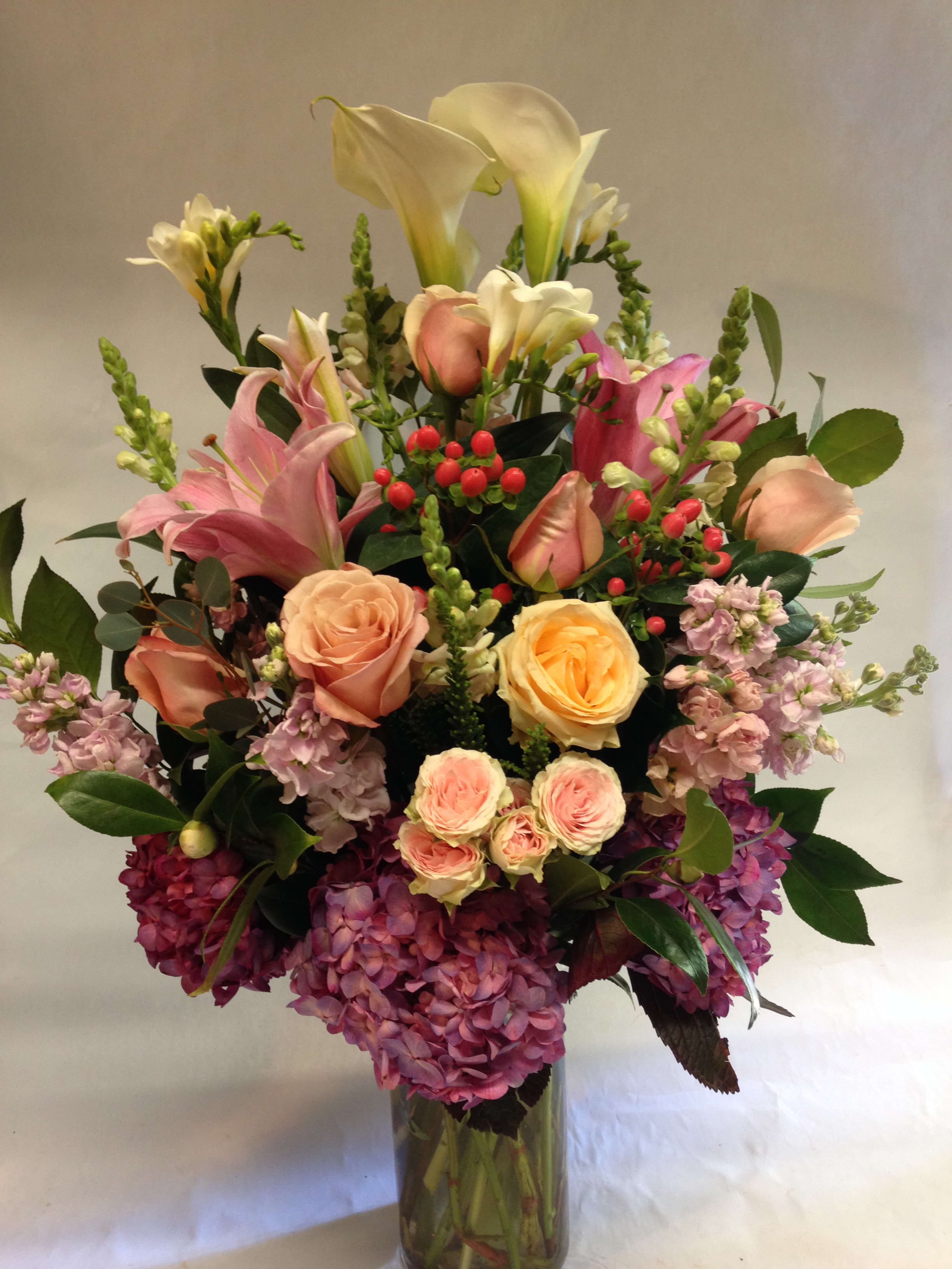 Blushing Beauty - This tall arrangement comes complete with white calla lilies, pink lilies, blush roses, blush spray roses, pink stock, pink hypericum, white snapdragons, lavender hydrangea and greenery.  (Some flowers may be subject to change depending on the season. We will contact you with available flower substitutions; please contact us with specific questions if you are concerned with flower availability, thanks!)  FEATURED ARRANGEMENT: $375.00 (Regular Price)