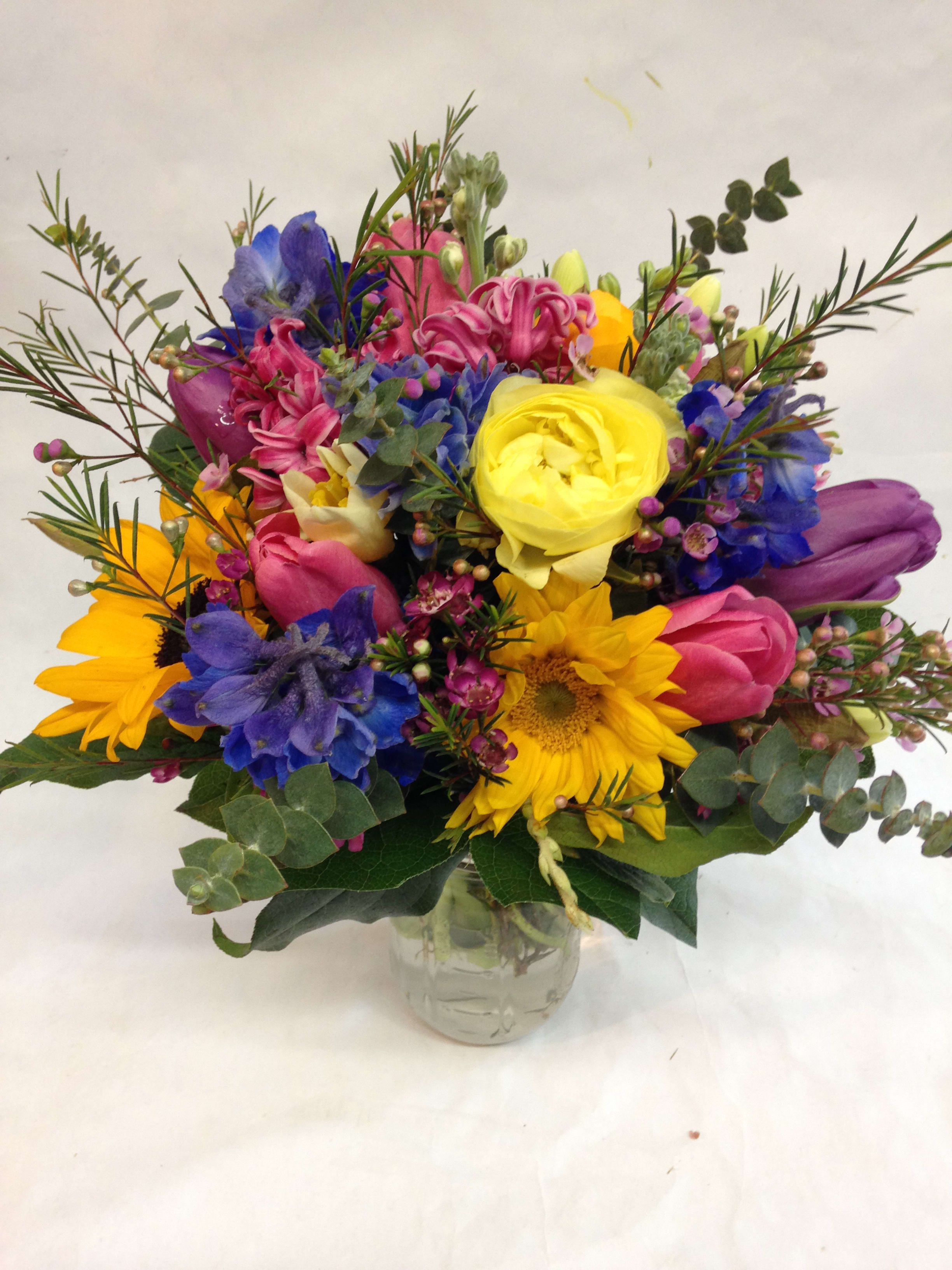 Colorful mixed bouquet in a clear glass vase with sunflowers and tulips