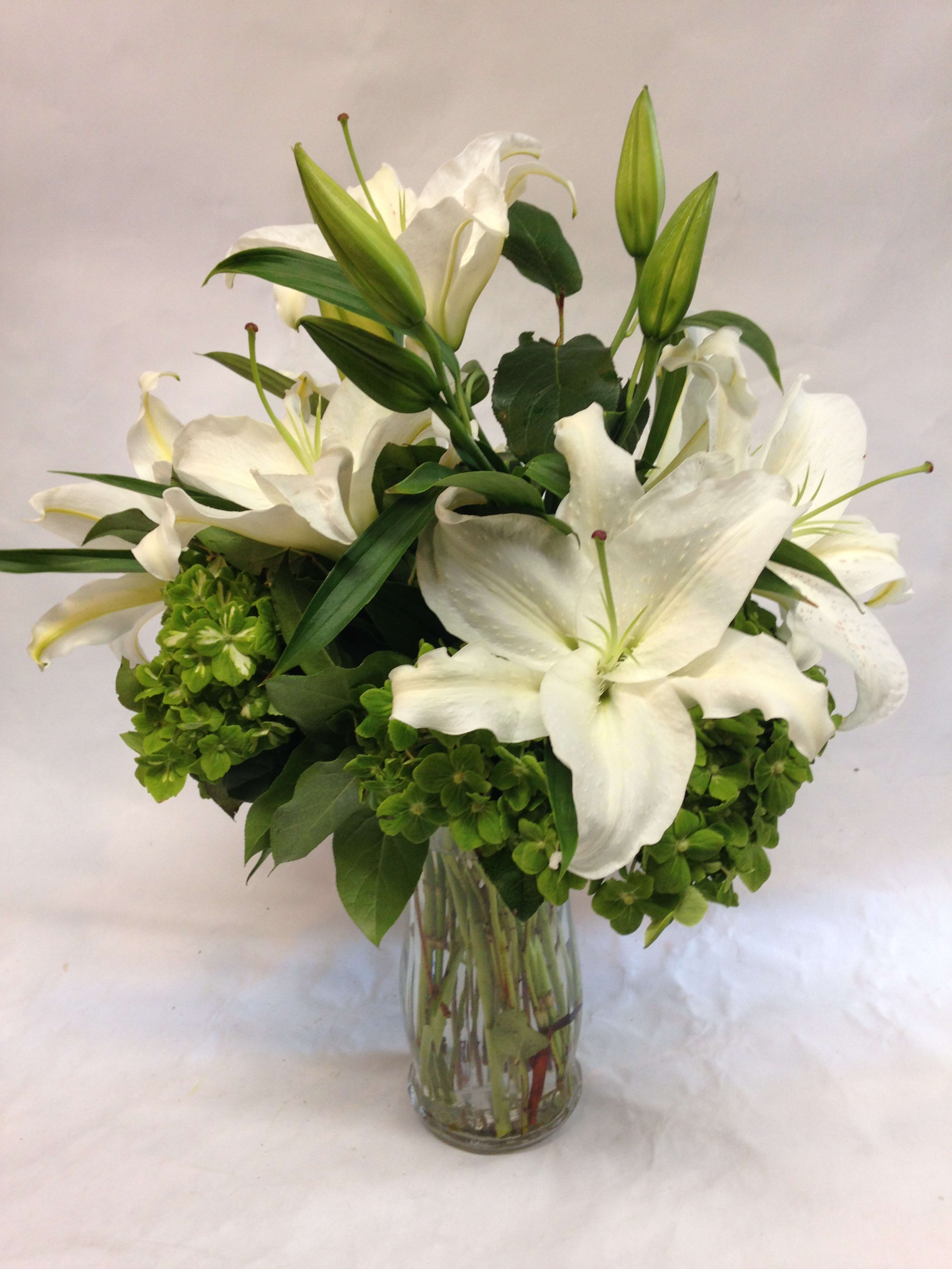 White lilies arranged in a clear glass vase with green blooms