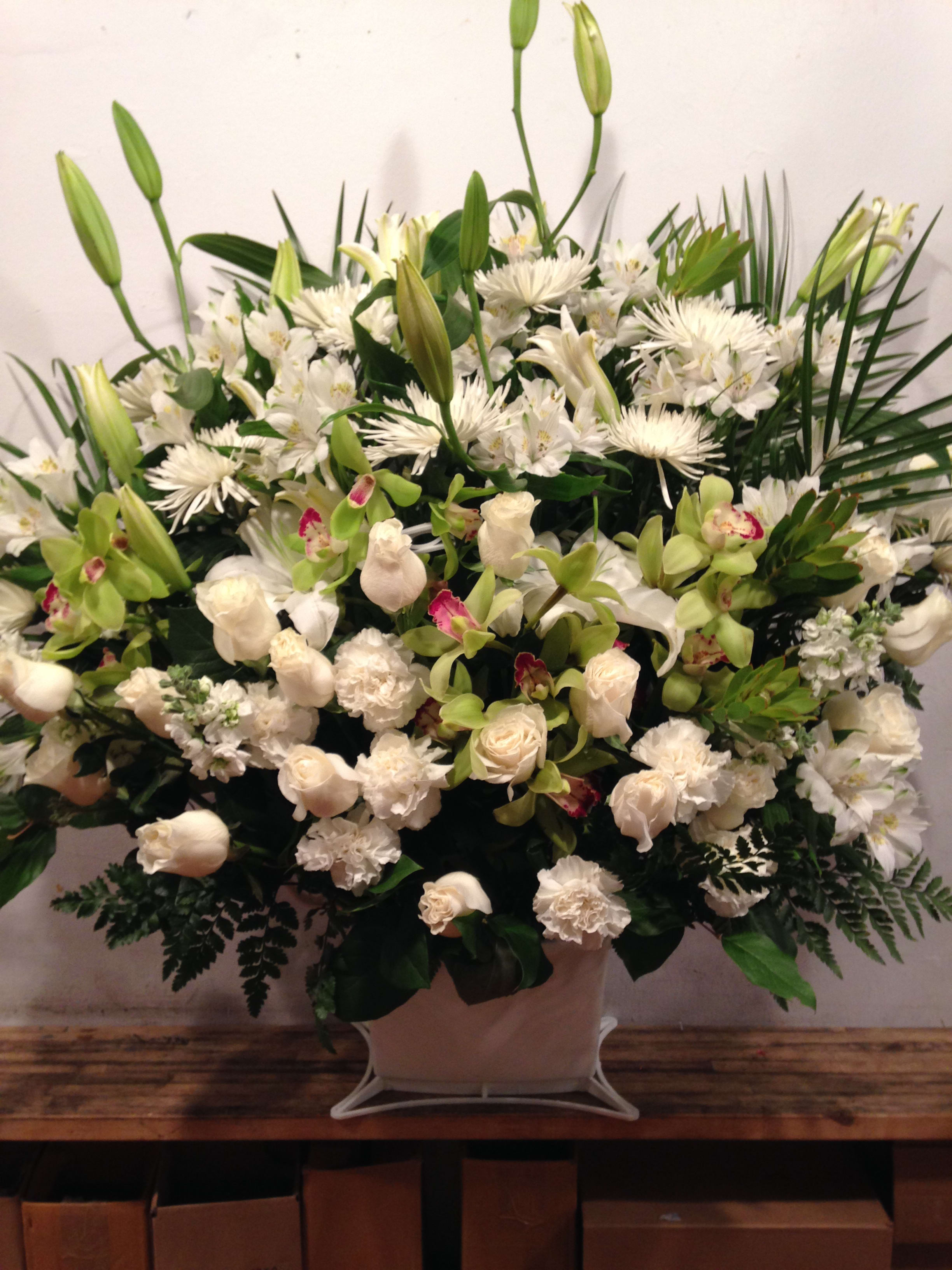 Large white floral arrangement with lilies, roses, and orchids in a pale vase