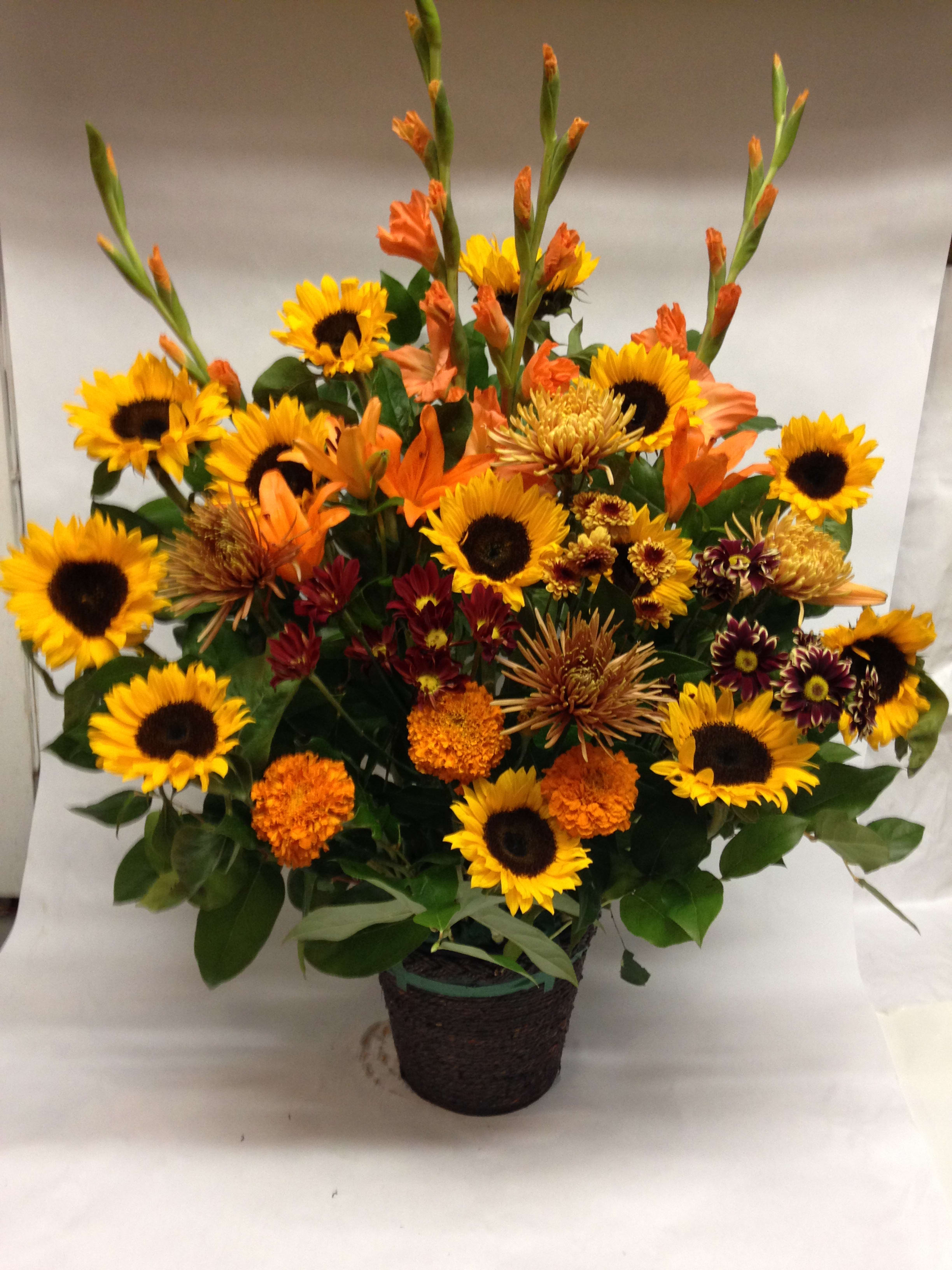 Mixed bouquet of sunflowers and orange flowers in a dark basket