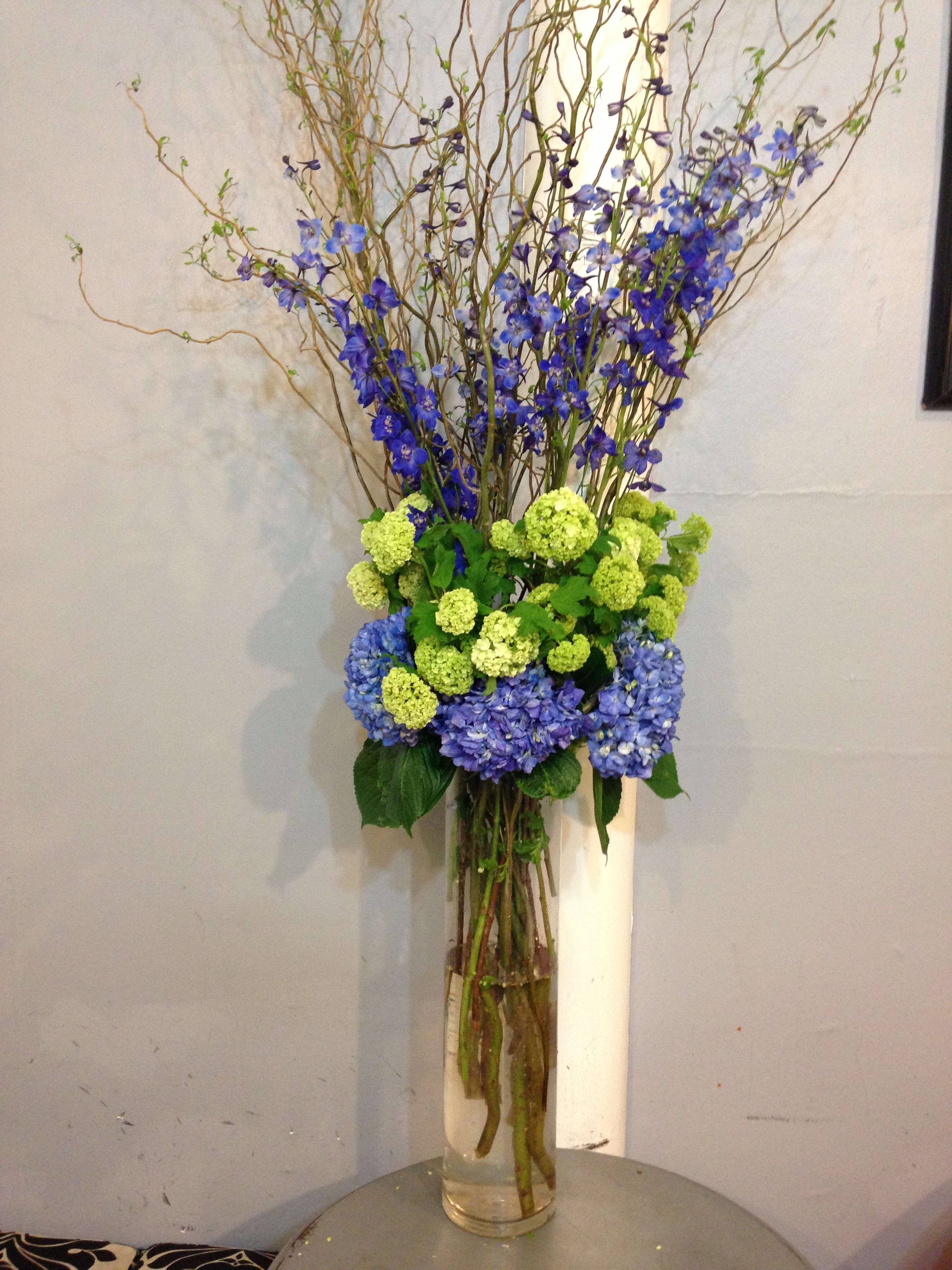 Tall blue and green floral arrangement in a clear glass vase