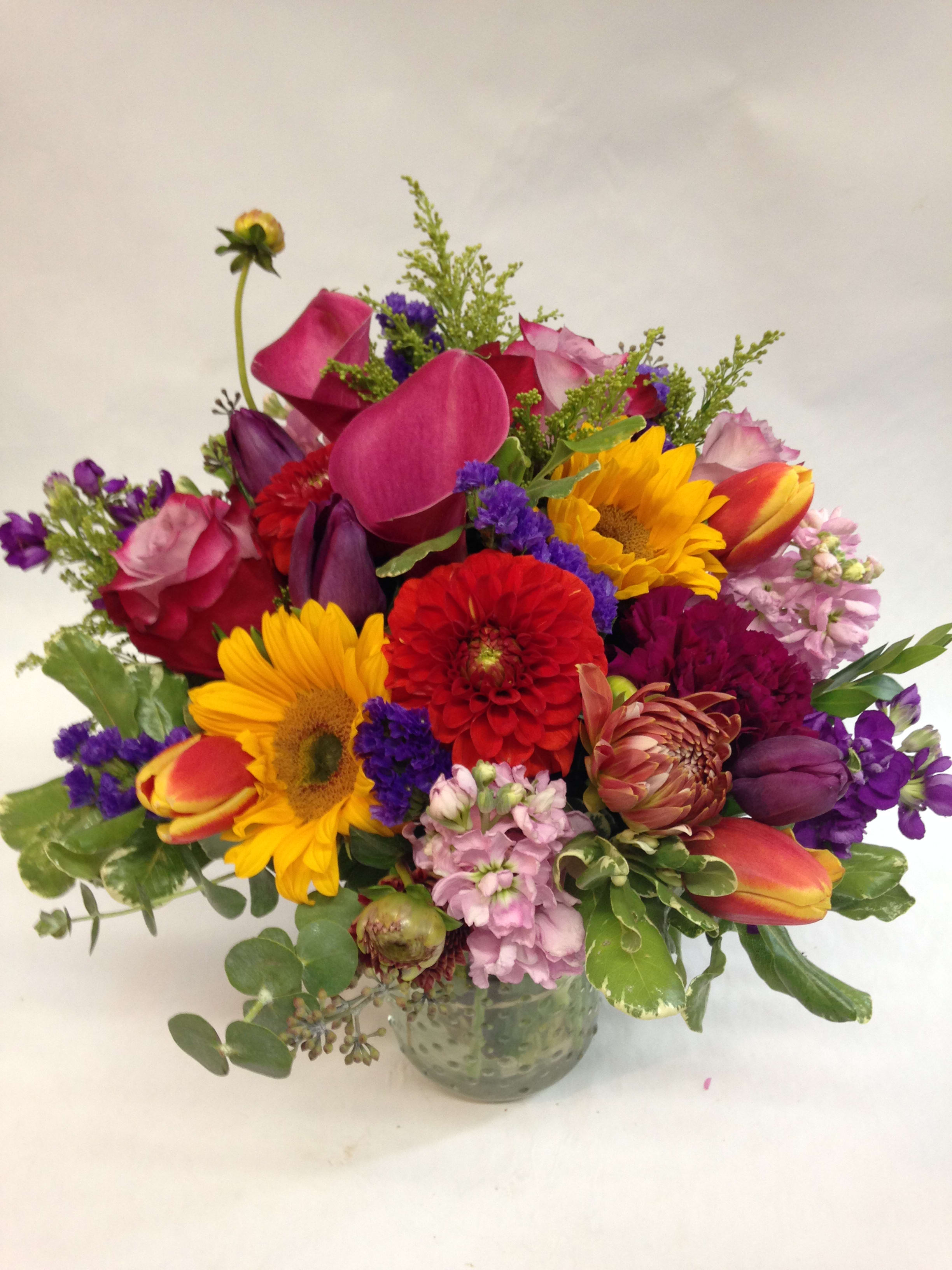 Mixed bouquet with sunflowers, tulips, roses, and calla lilies in a glass vase