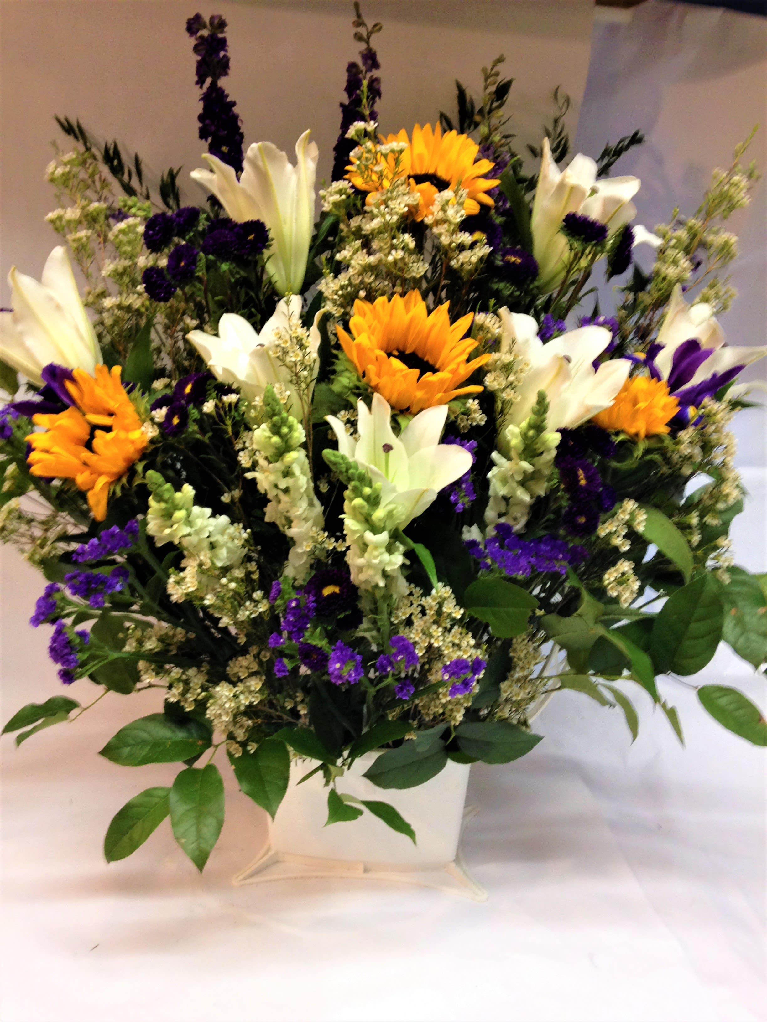 Bouquet of white lilies, sunflowers, and purple flowers in a white vase