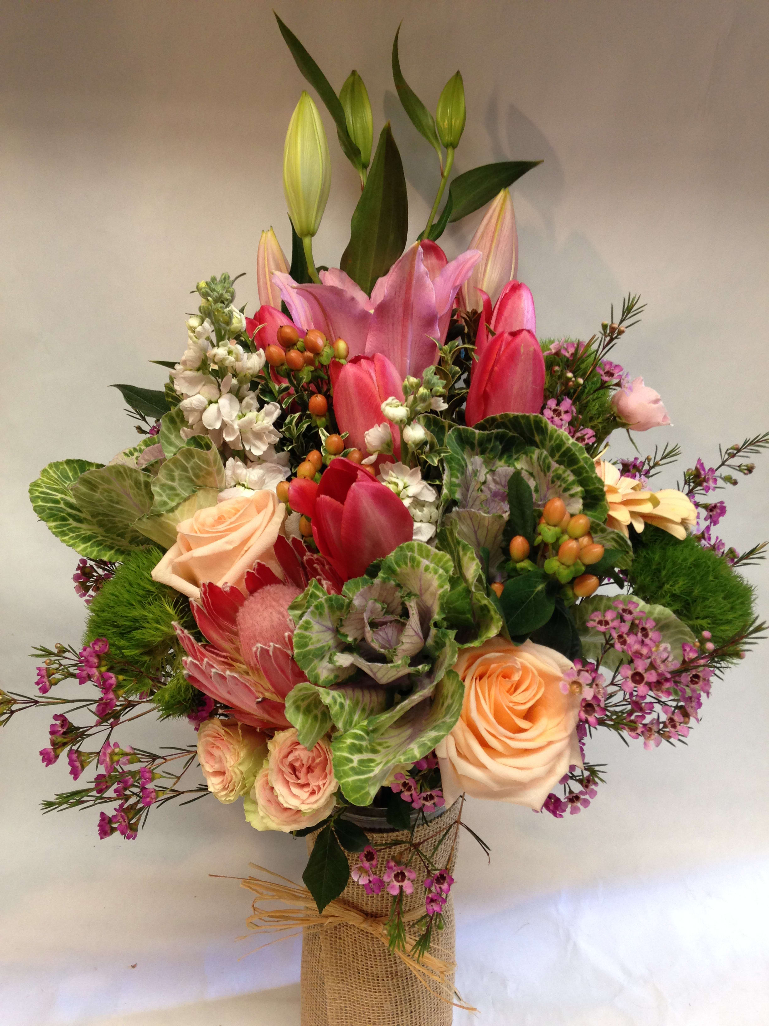 Mixed bouquet with pink lilies, roses, and tulips in a wrapped vase