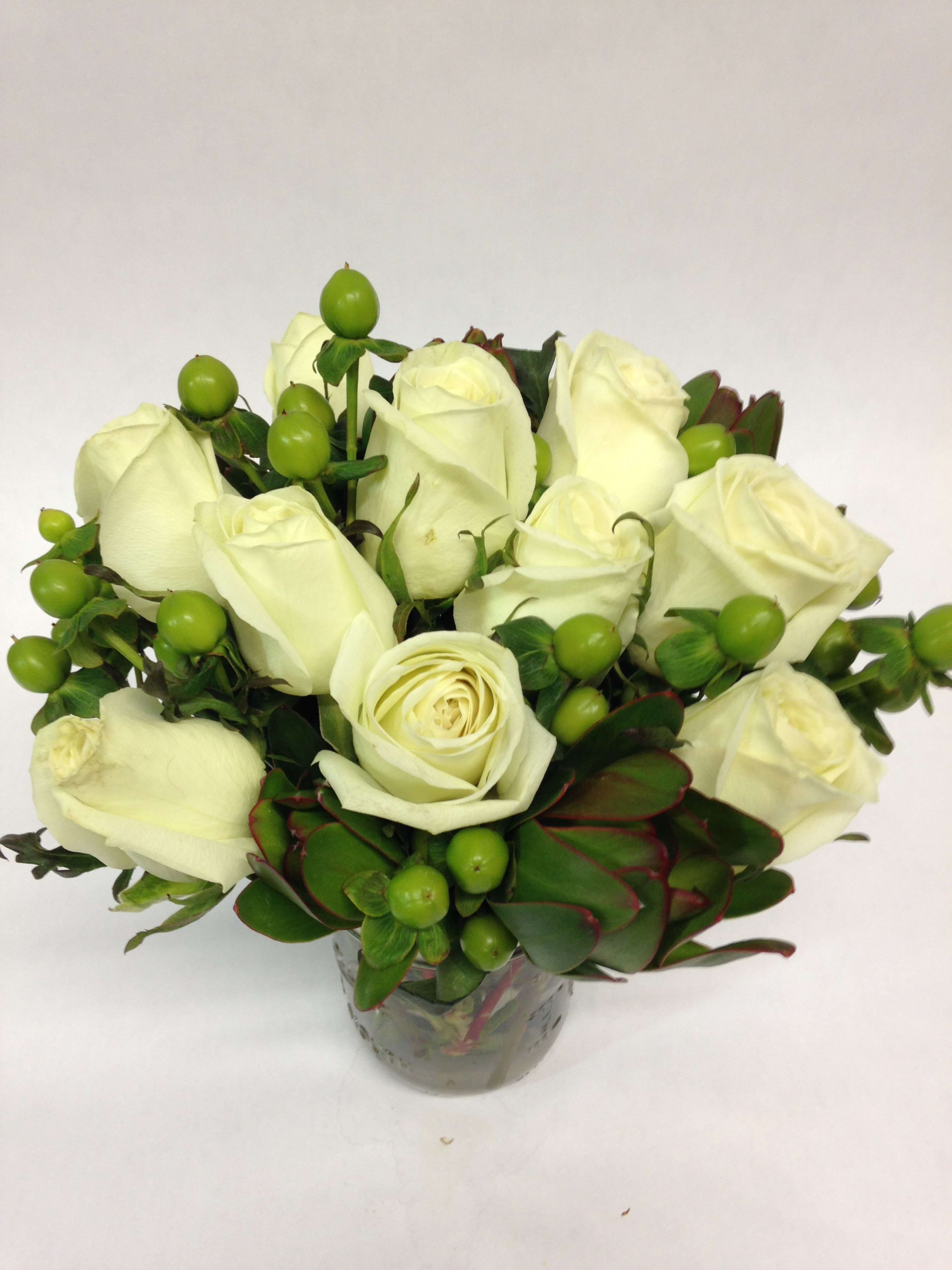 White rose bouquet in a glass vase with green berries