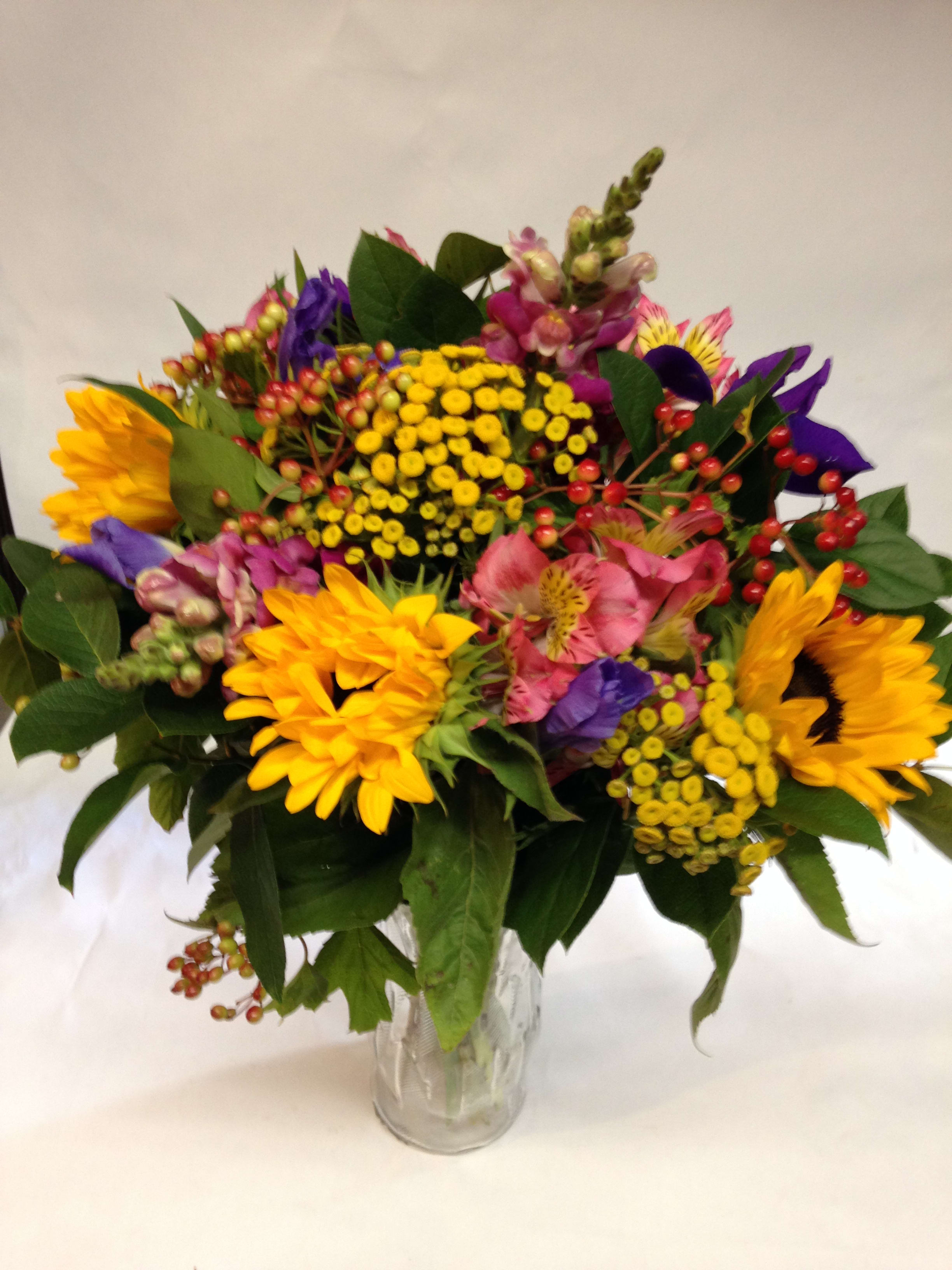 Mixed bouquet of sunflowers, pink blooms, and yellow filler flowers in a glass vase