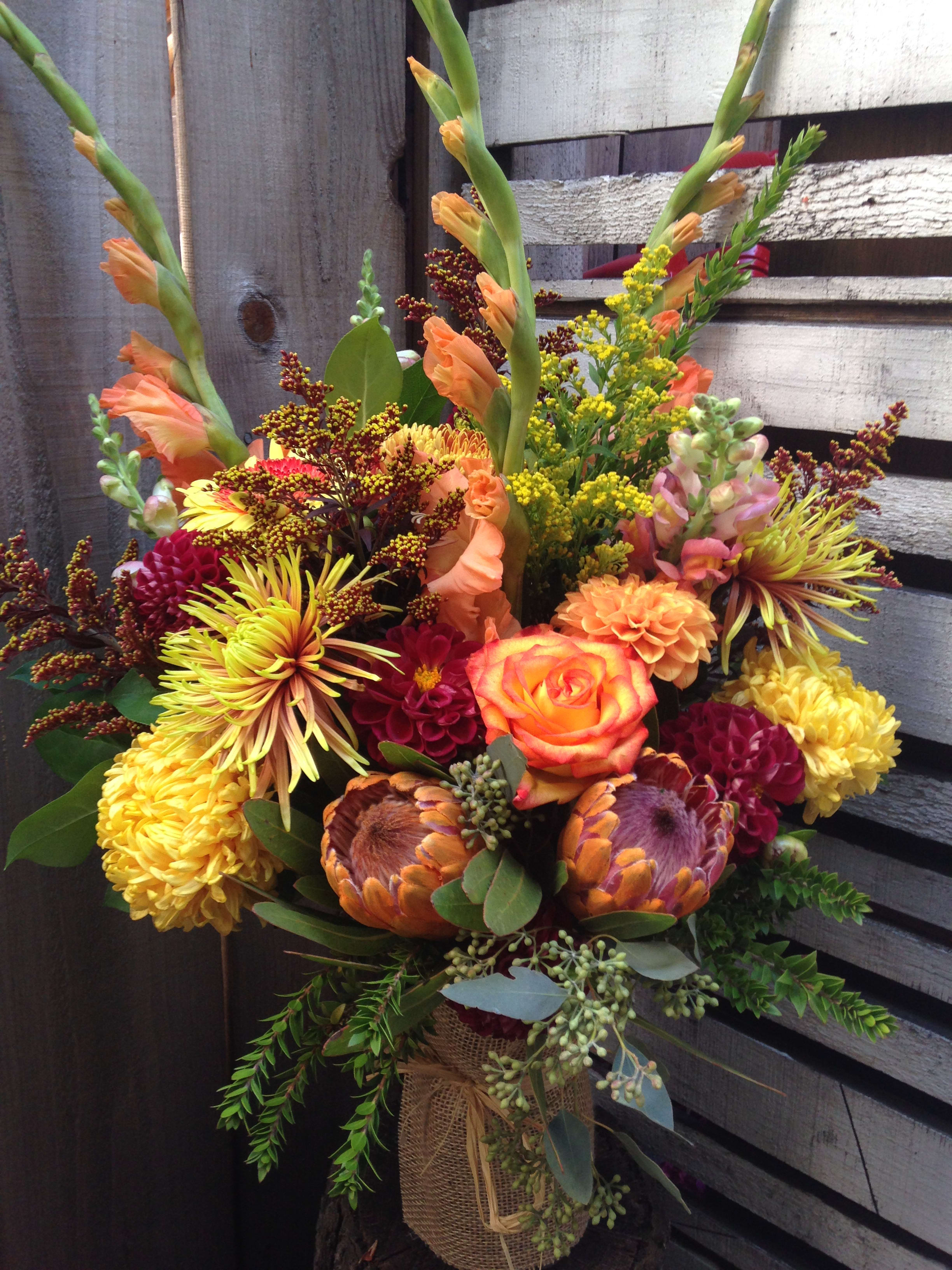 Colorful bouquet with orange roses and yellow chrysanthemums in a burlap-wrapped vase