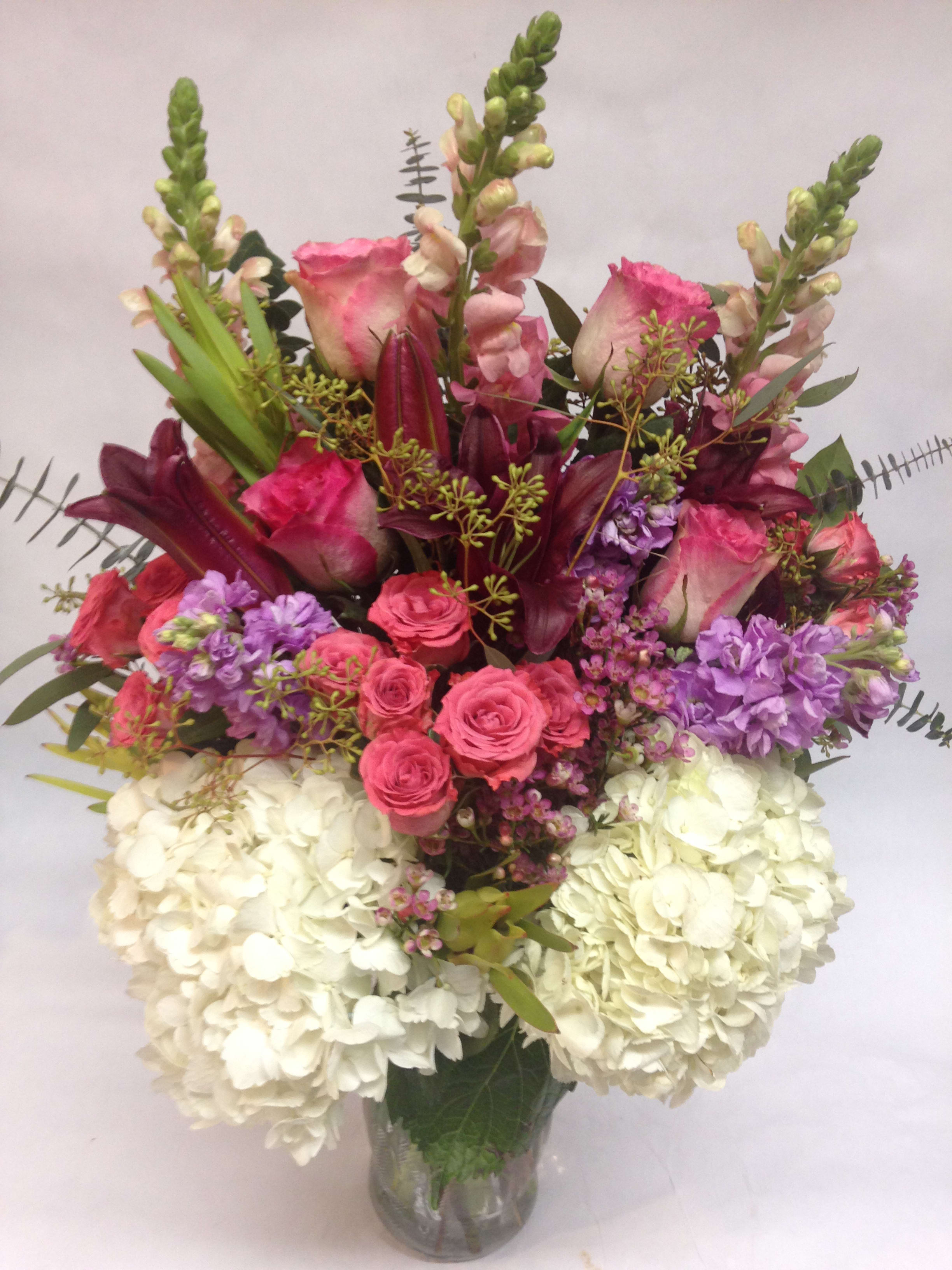 Mixed bouquet of pink roses, purple flowers, and white hydrangeas in a glass vase