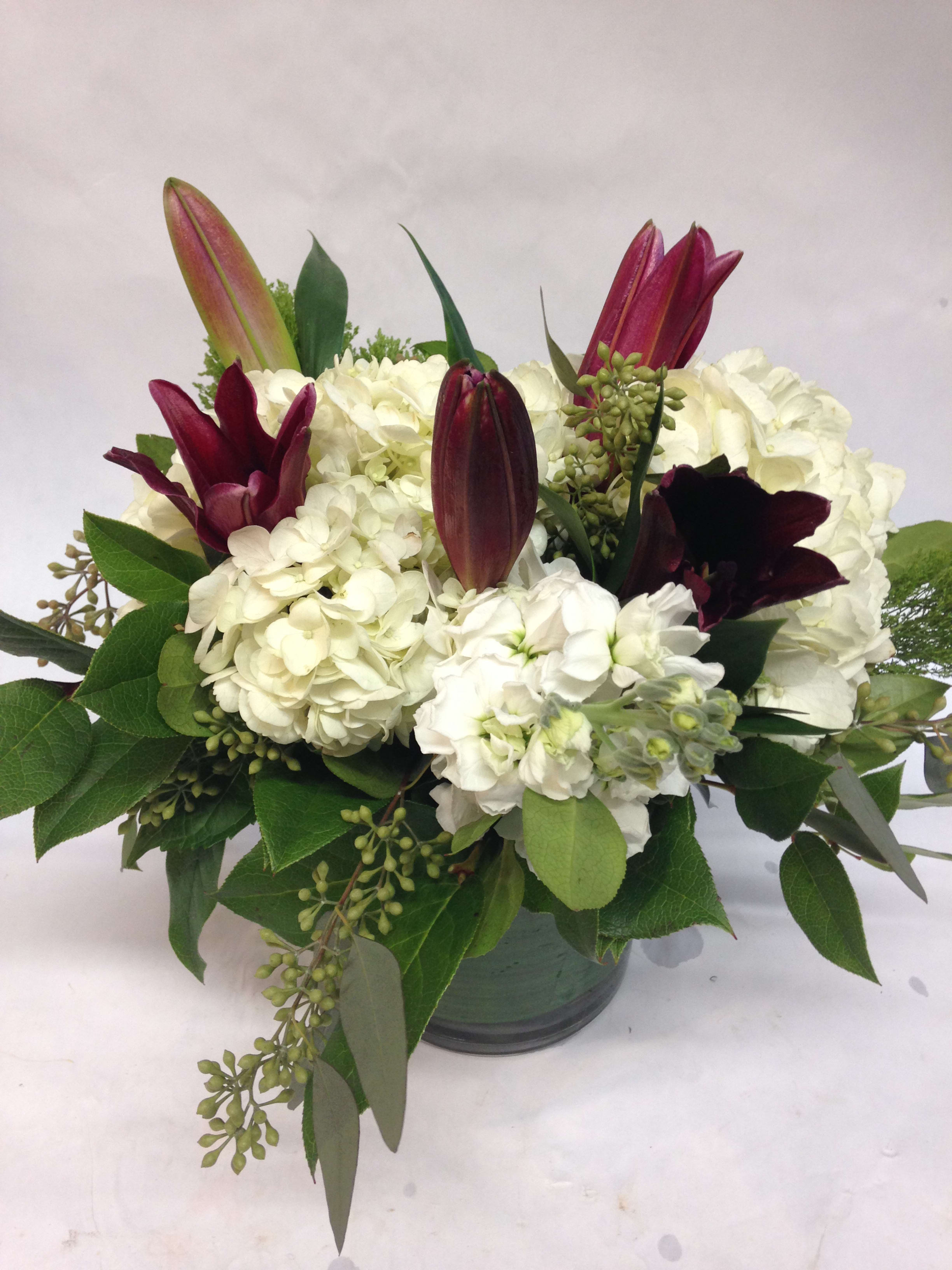 White hydrangeas with burgundy lilies in a glass vase