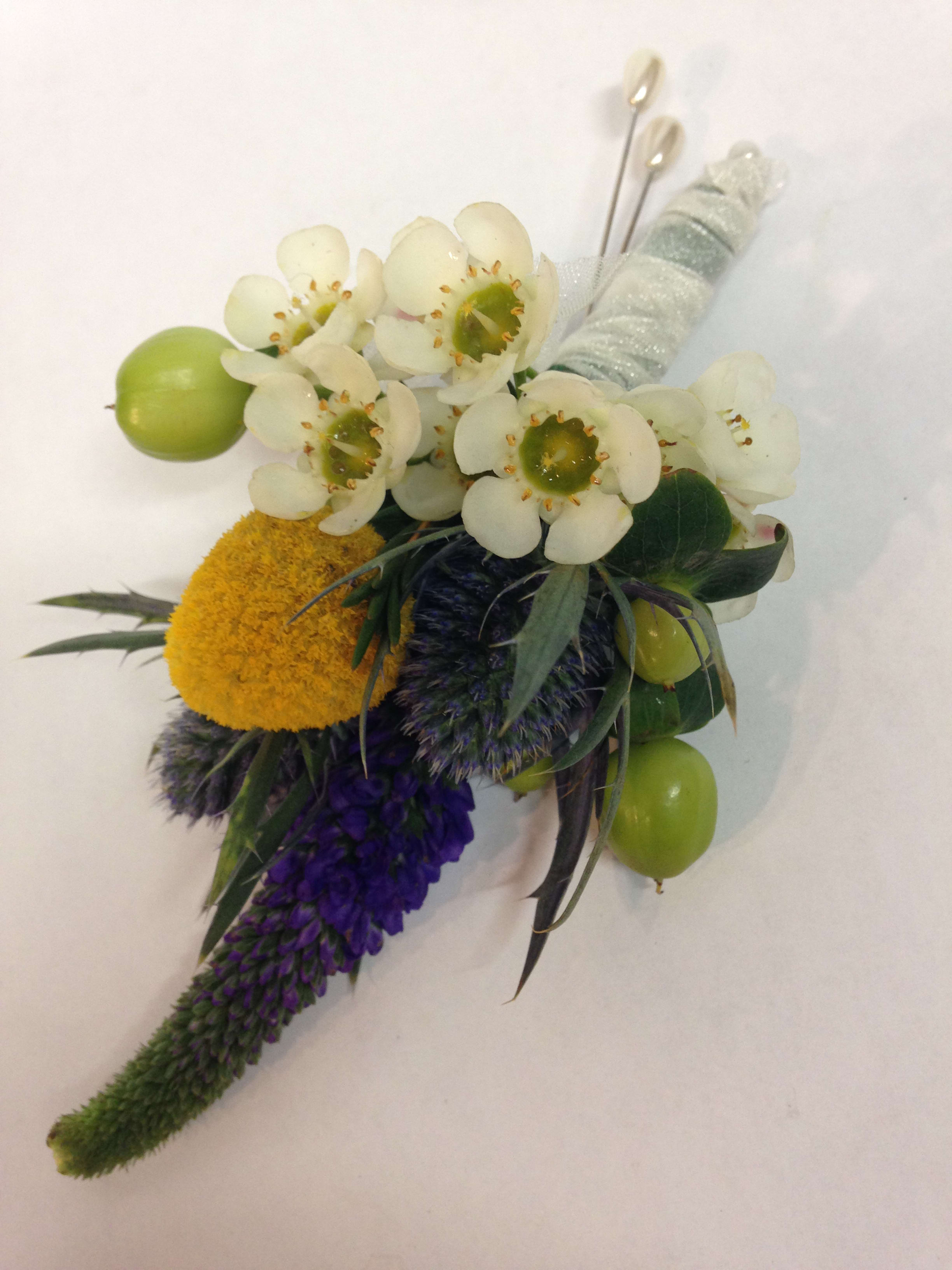 Boutonniere with white blossoms, green berries, and purple accents