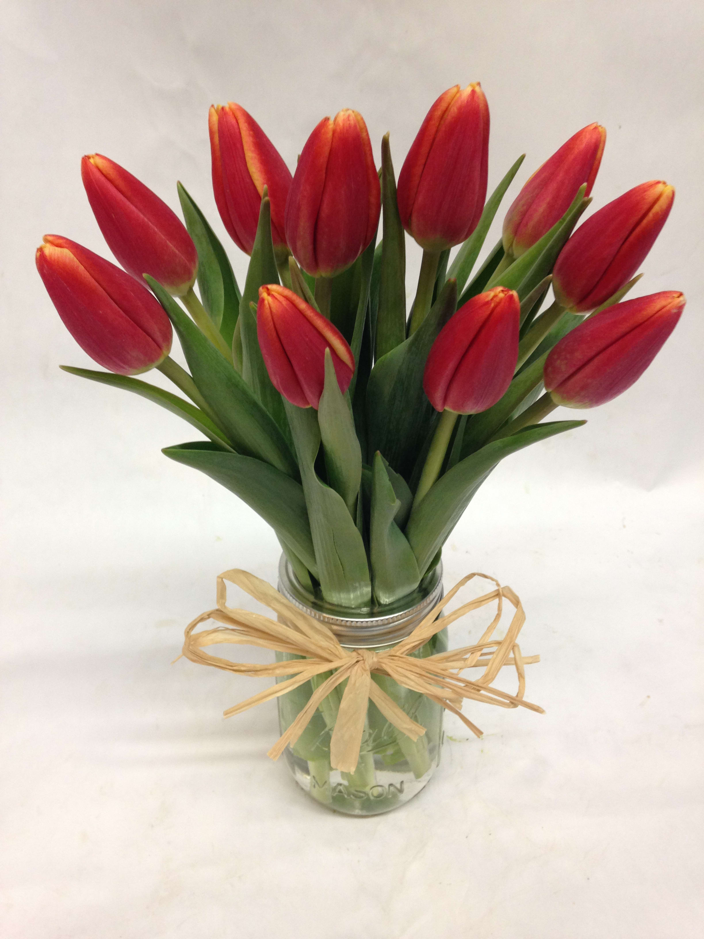 Red tulips in a glass jar tied with a raffia bow
