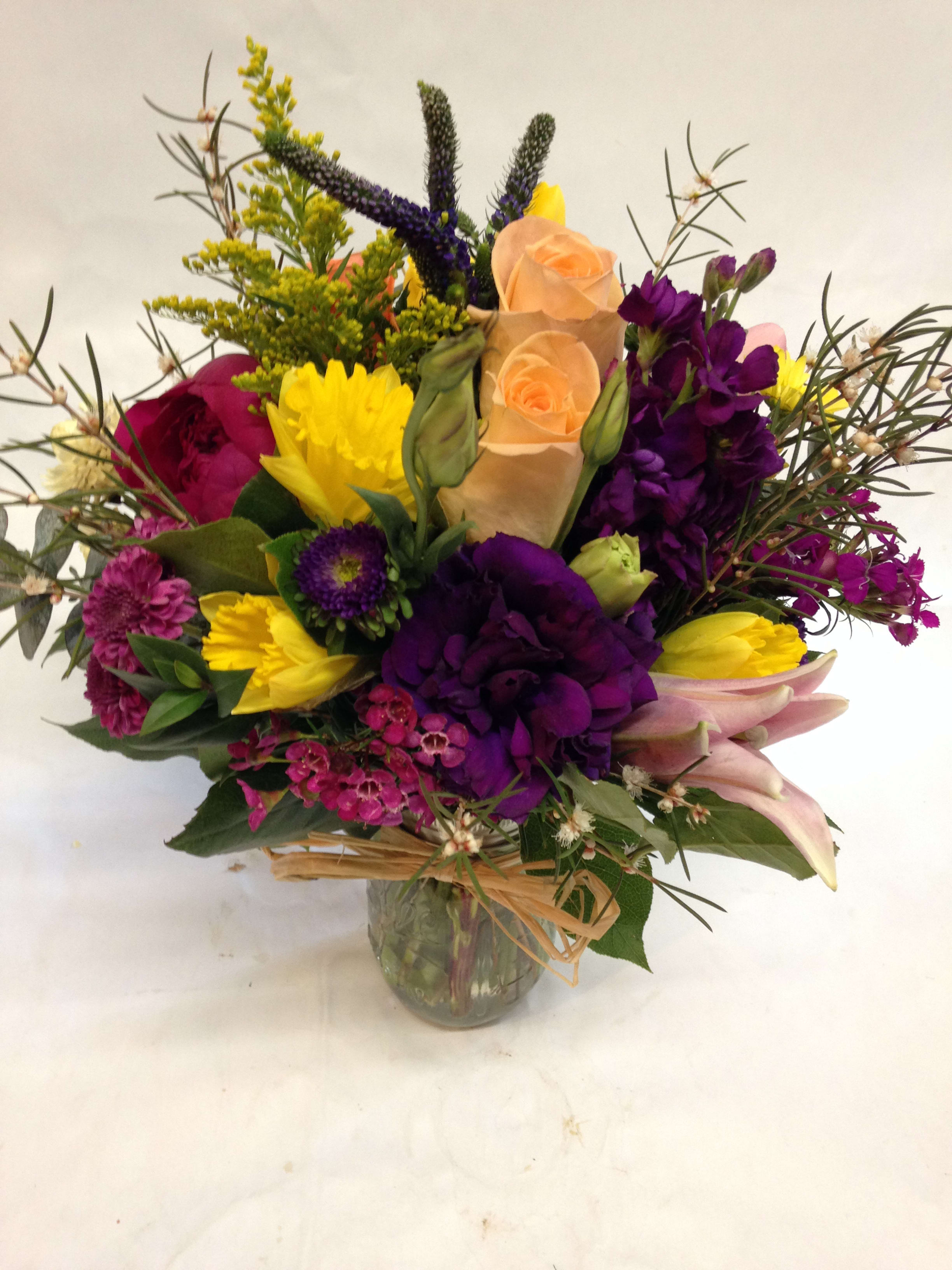 Mixed bouquet of purple, yellow, and peach flowers in a glass vase