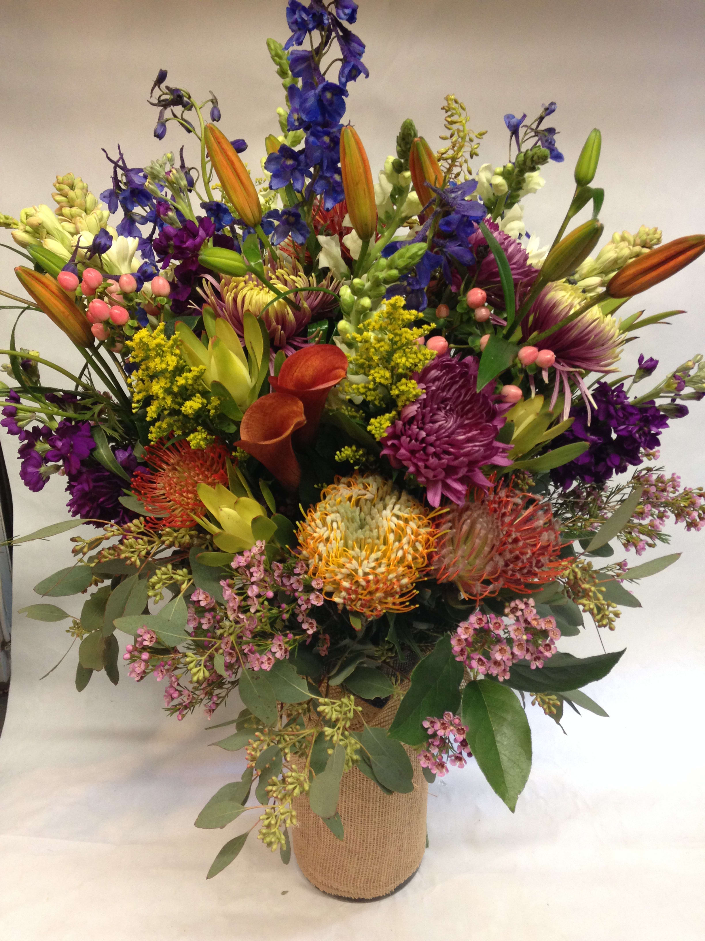 Mixed bouquet with lilies, calla lilies, and purple blooms in a burlap-wrapped vase