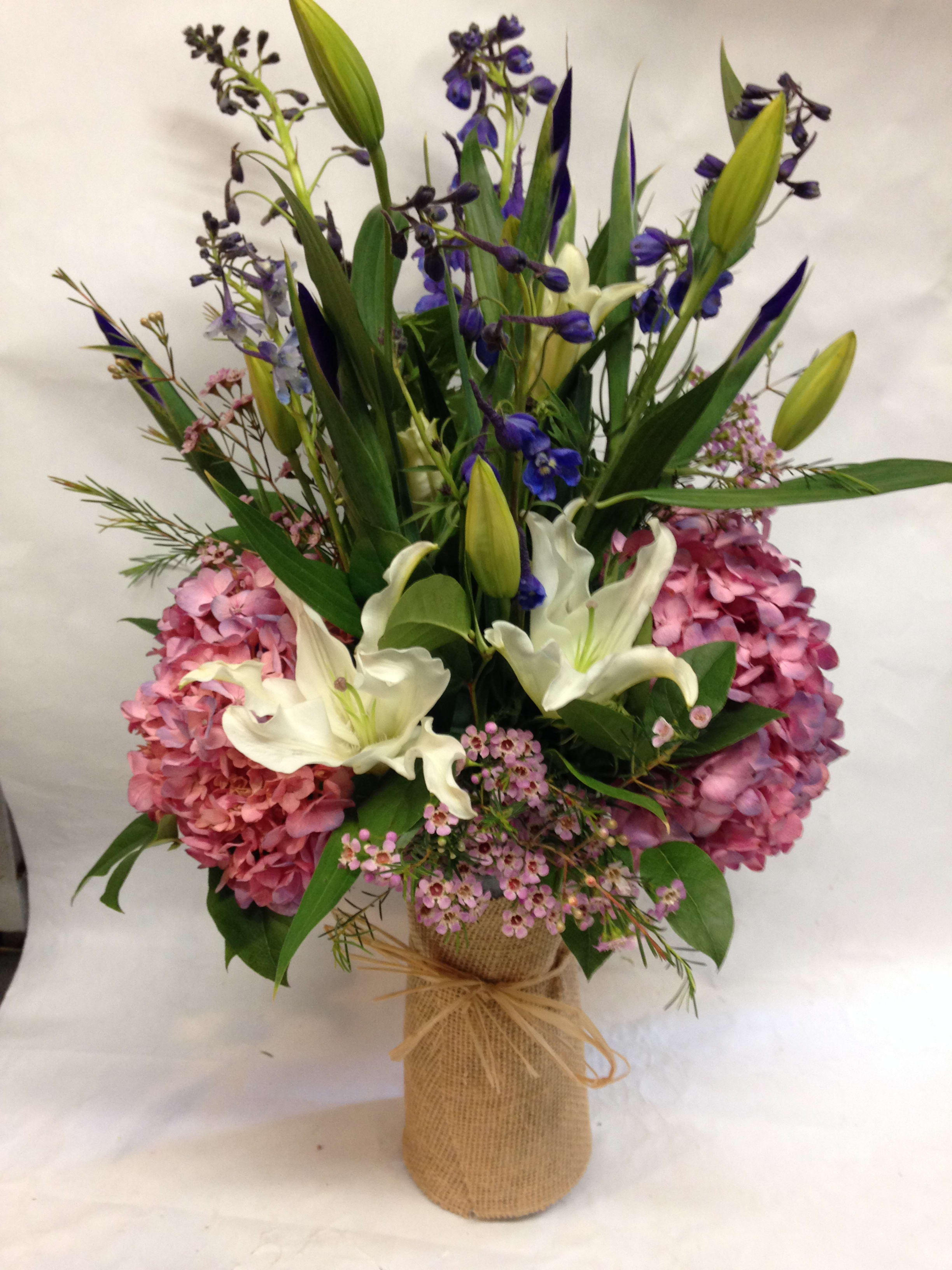 Bouquet of pink hydrangeas, white lilies, and purple flowers in a burlap-wrapped vase