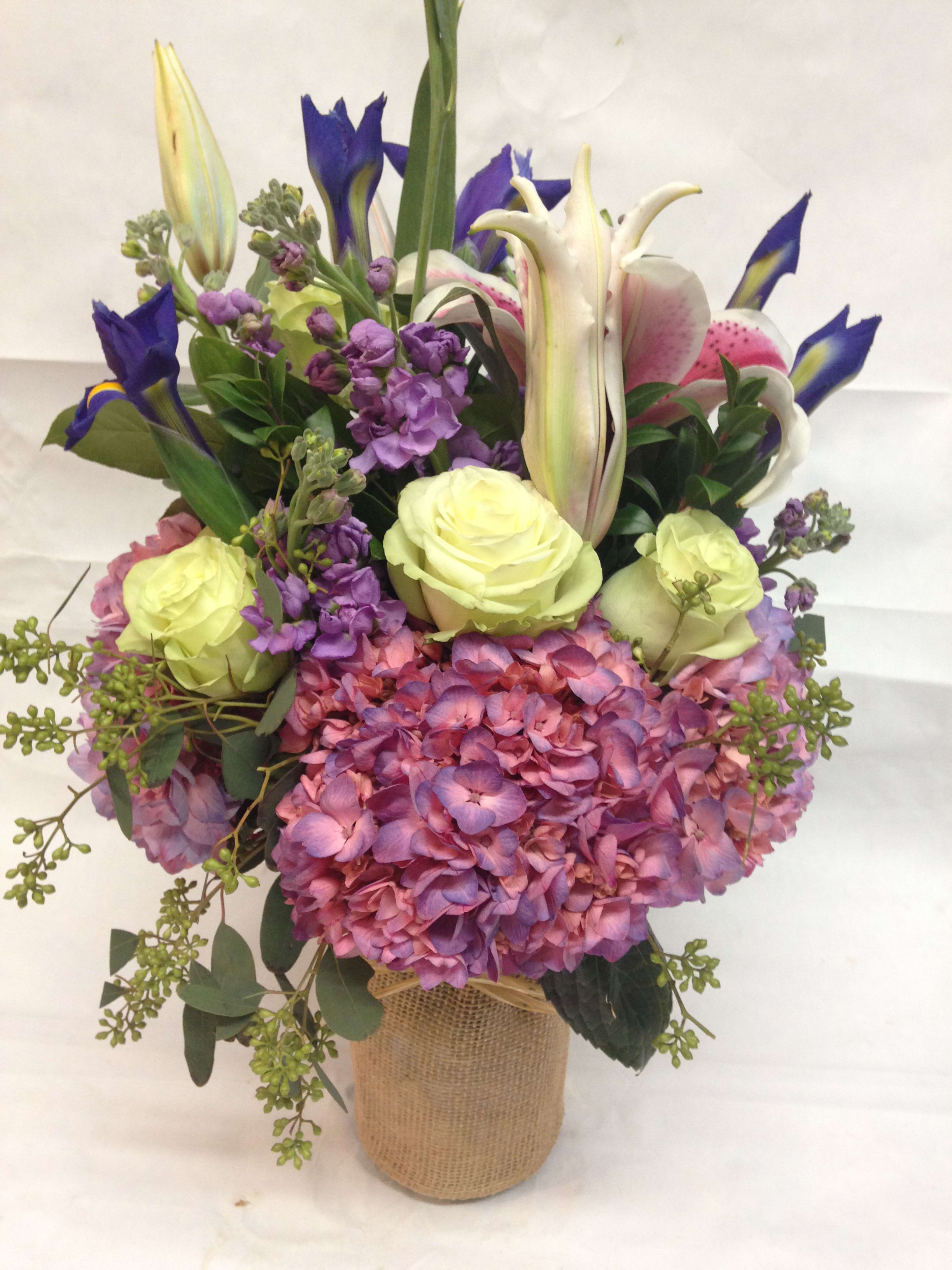 Bouquet of pink hydrangeas, lilies, irises, and pale roses in a burlap-wrapped vase