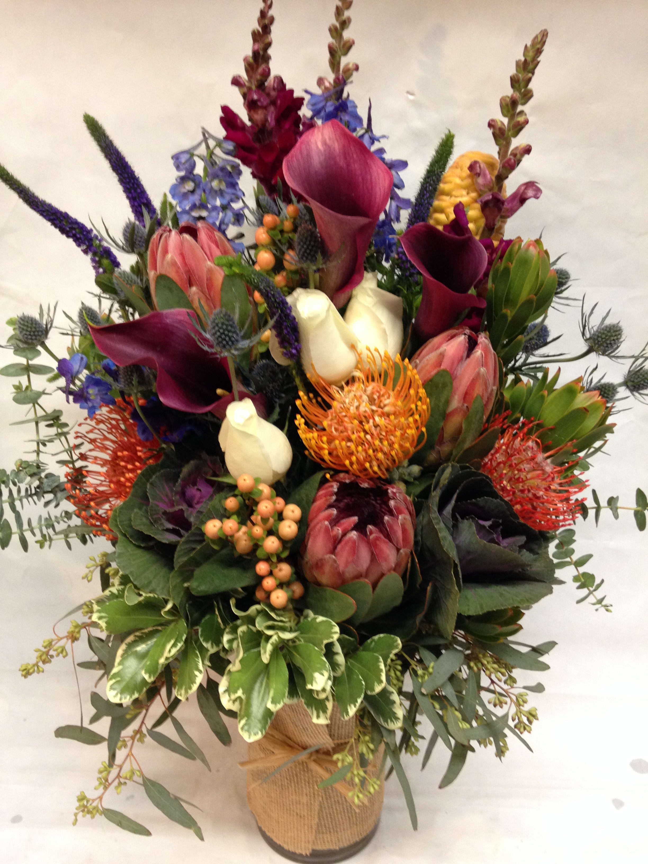Mixed bouquet with calla lilies, protea, and purple spikes in a wrapped vase