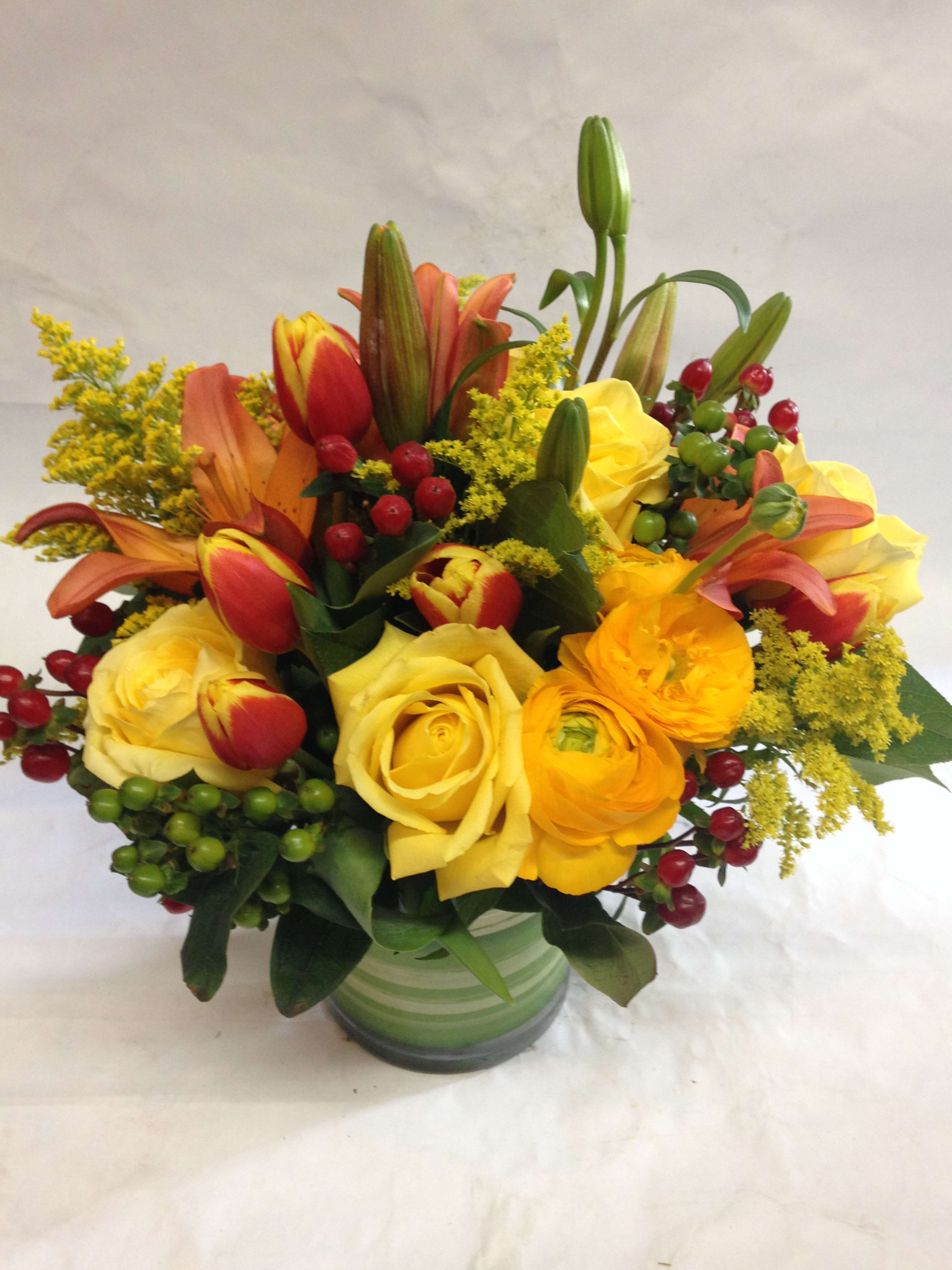 Bouquet of yellow roses, tulips, and lilies in a green striped vase