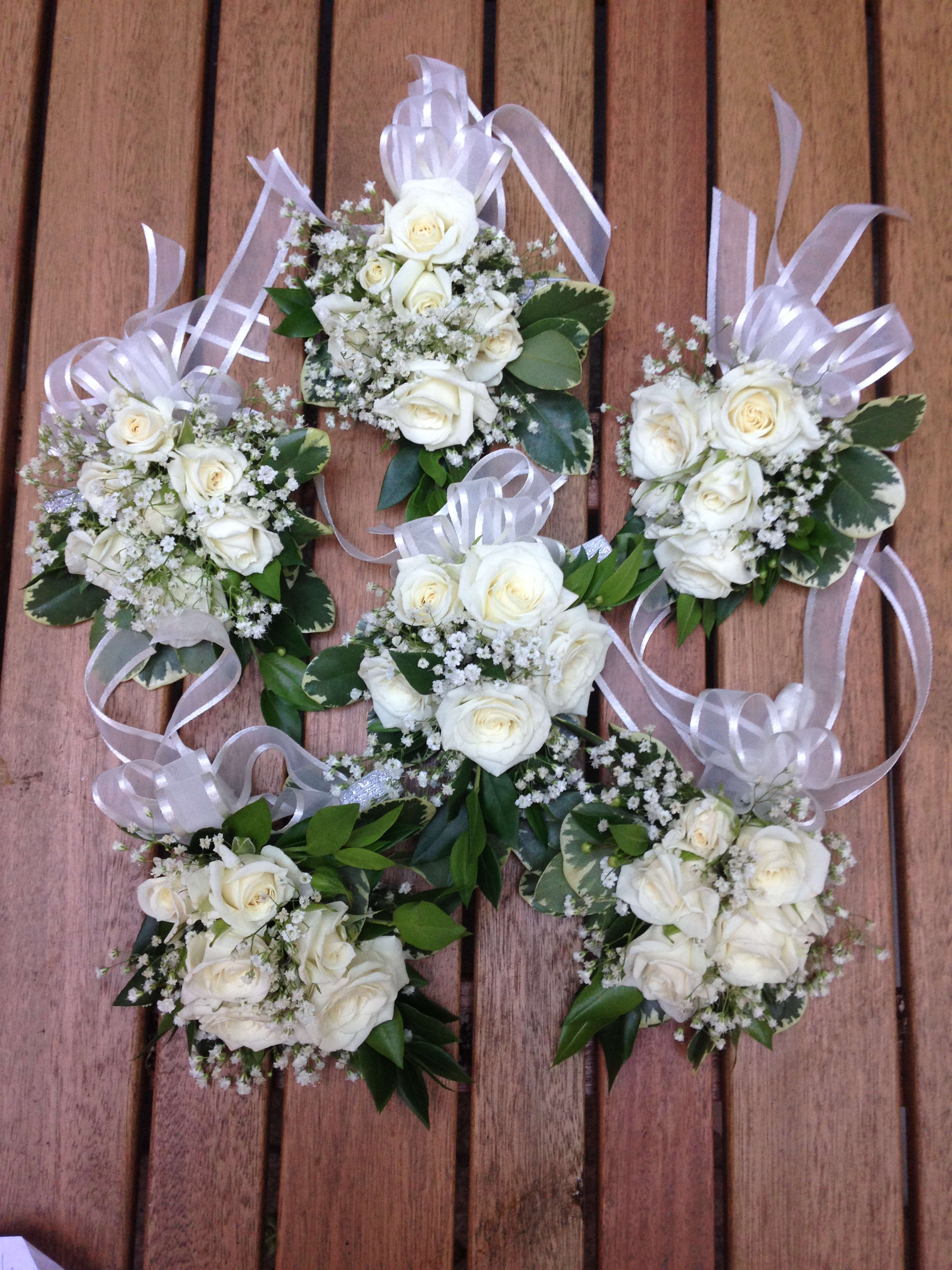 White rose corsages with ribbon bows on a wooden surface