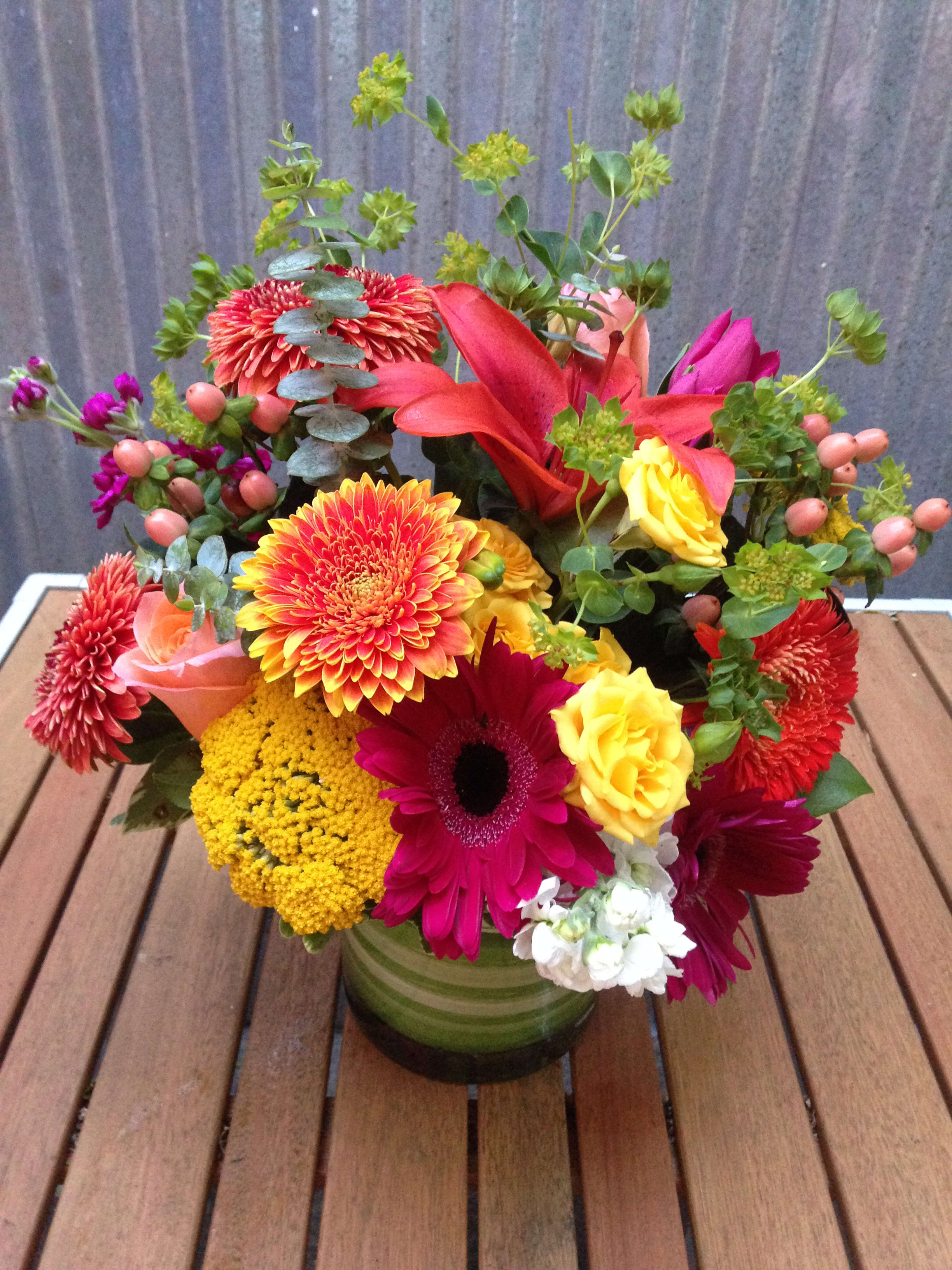 Colorful mixed bouquet in a green glass vase with roses and daisies