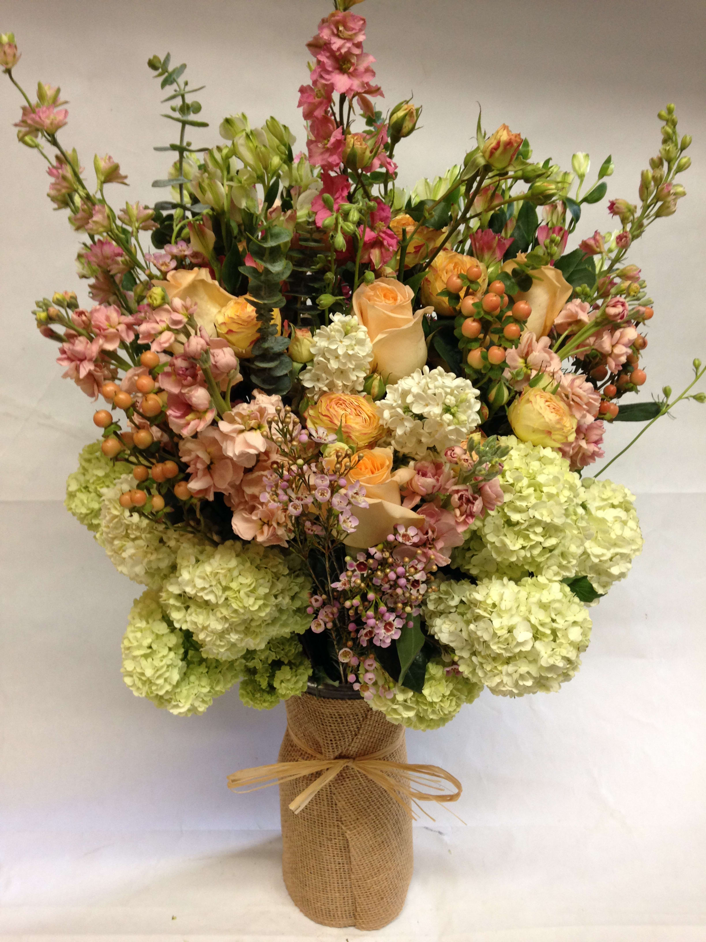 Tall mixed bouquet in a burlap-wrapped vase with peach, pink, and green blooms