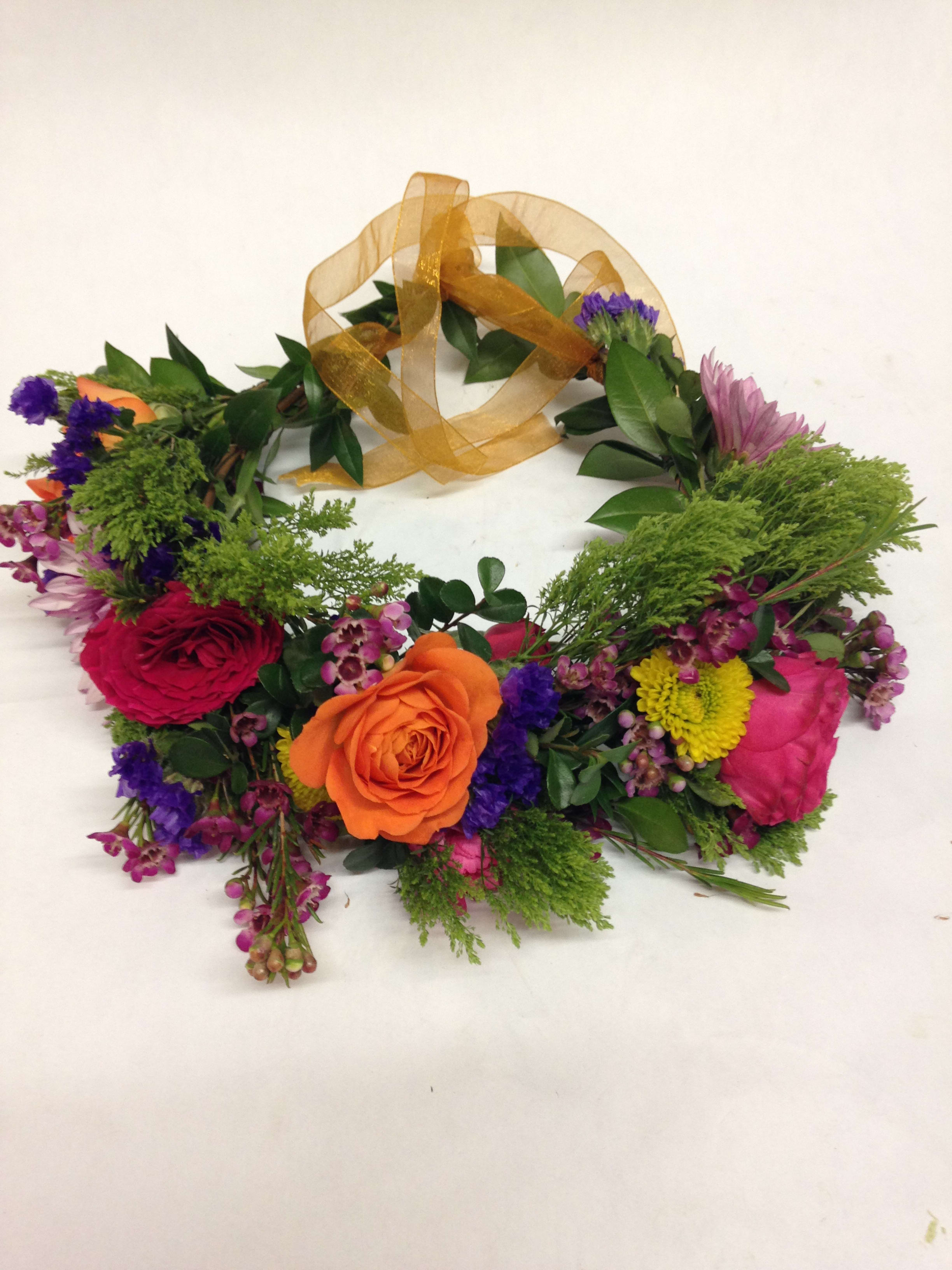 Floral wreath with roses and mixed blooms tied with a gold ribbon