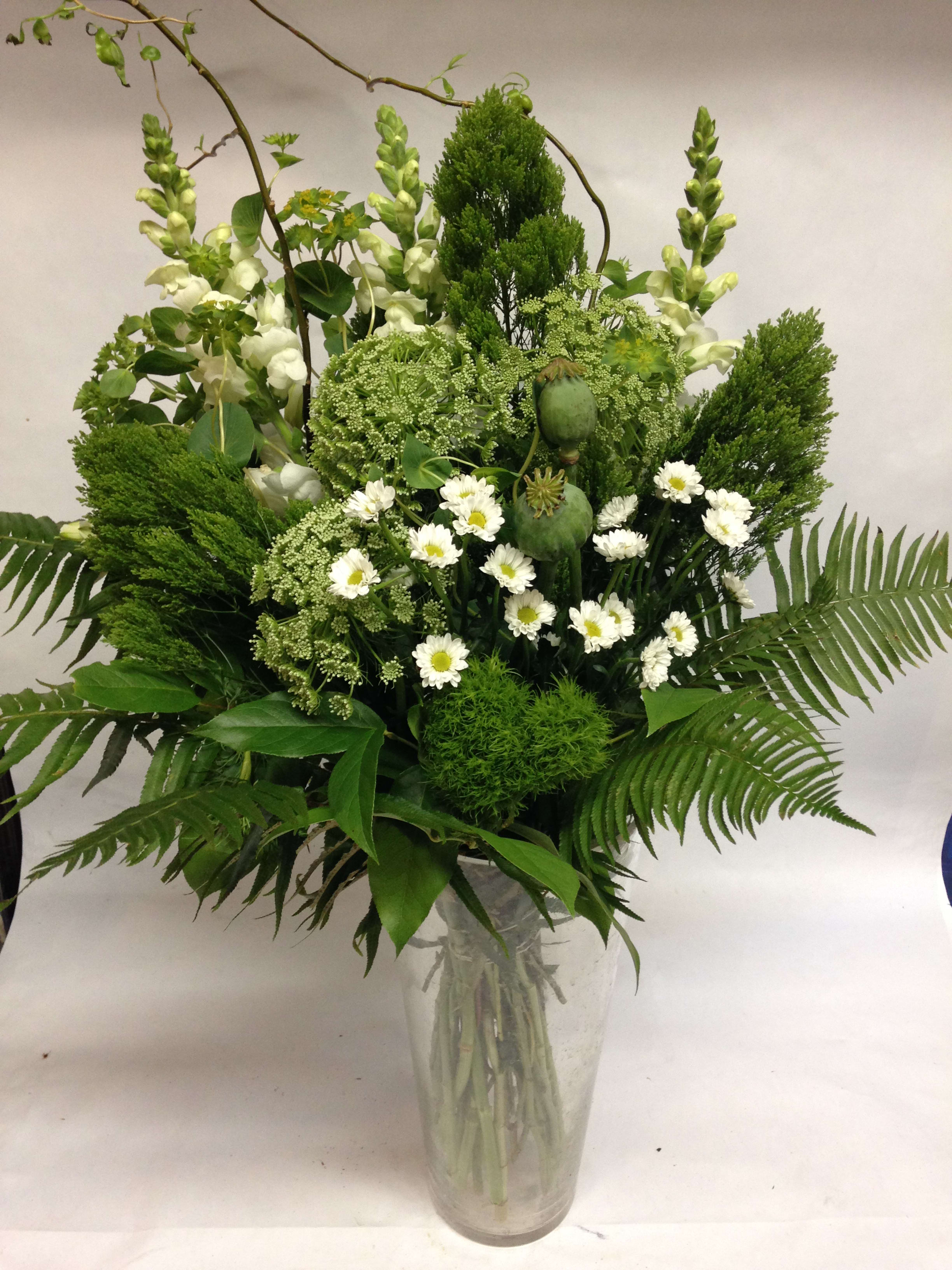 Tall green bouquet with white daisies in a clear glass vase