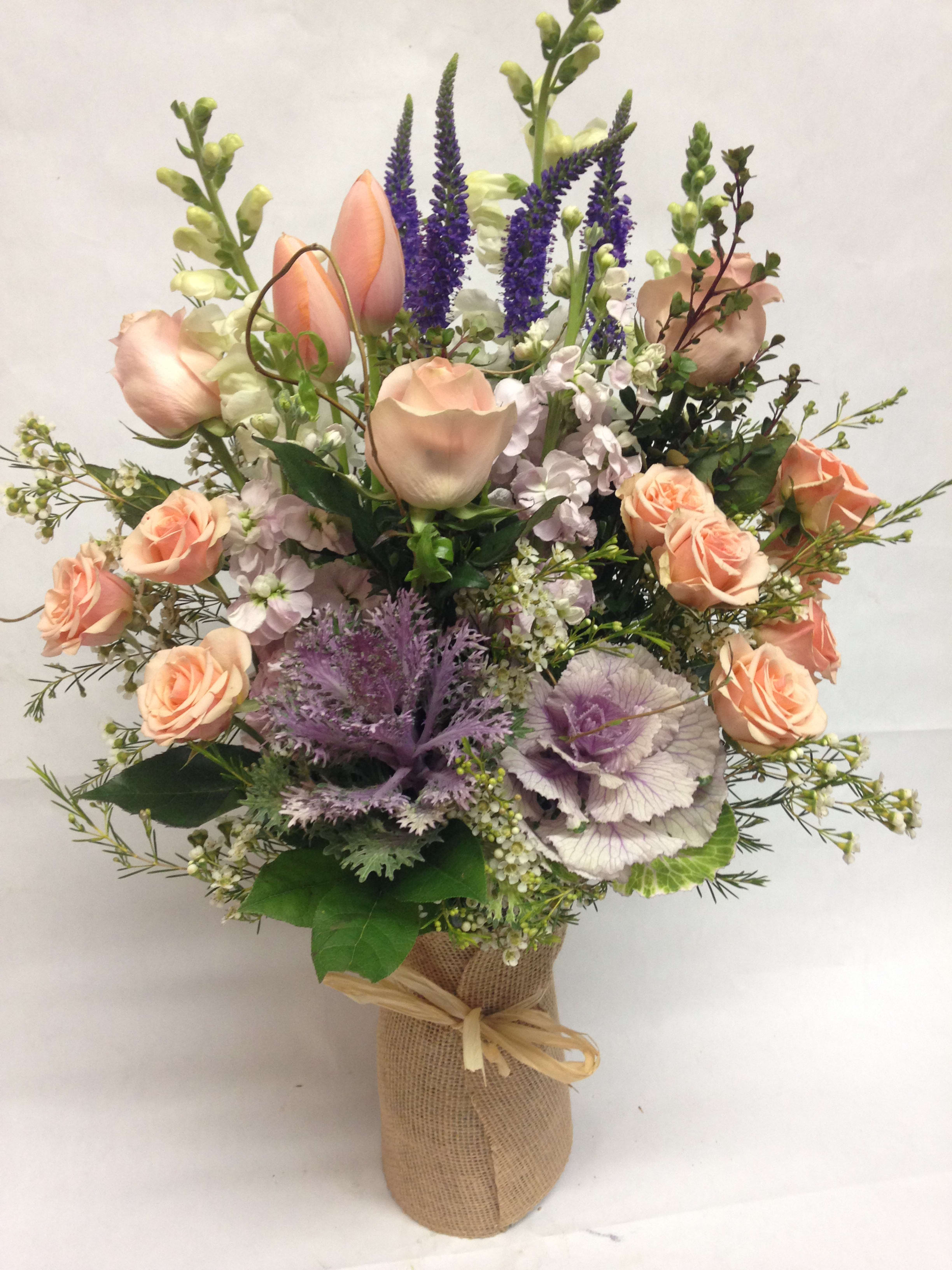Peach roses and purple flowers arranged in a burlap-wrapped vase
