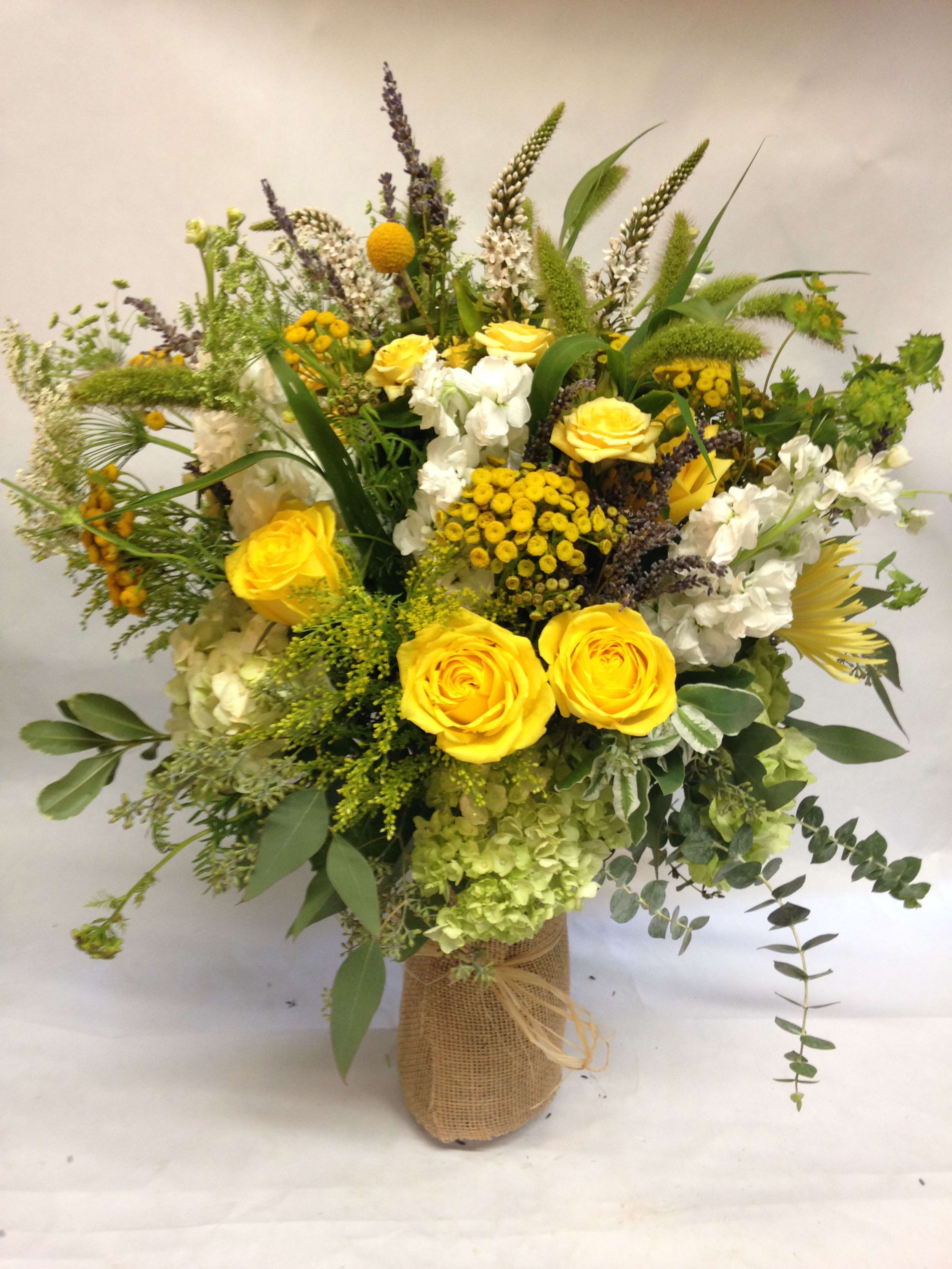 Yellow roses and white flowers in a burlap-wrapped vase