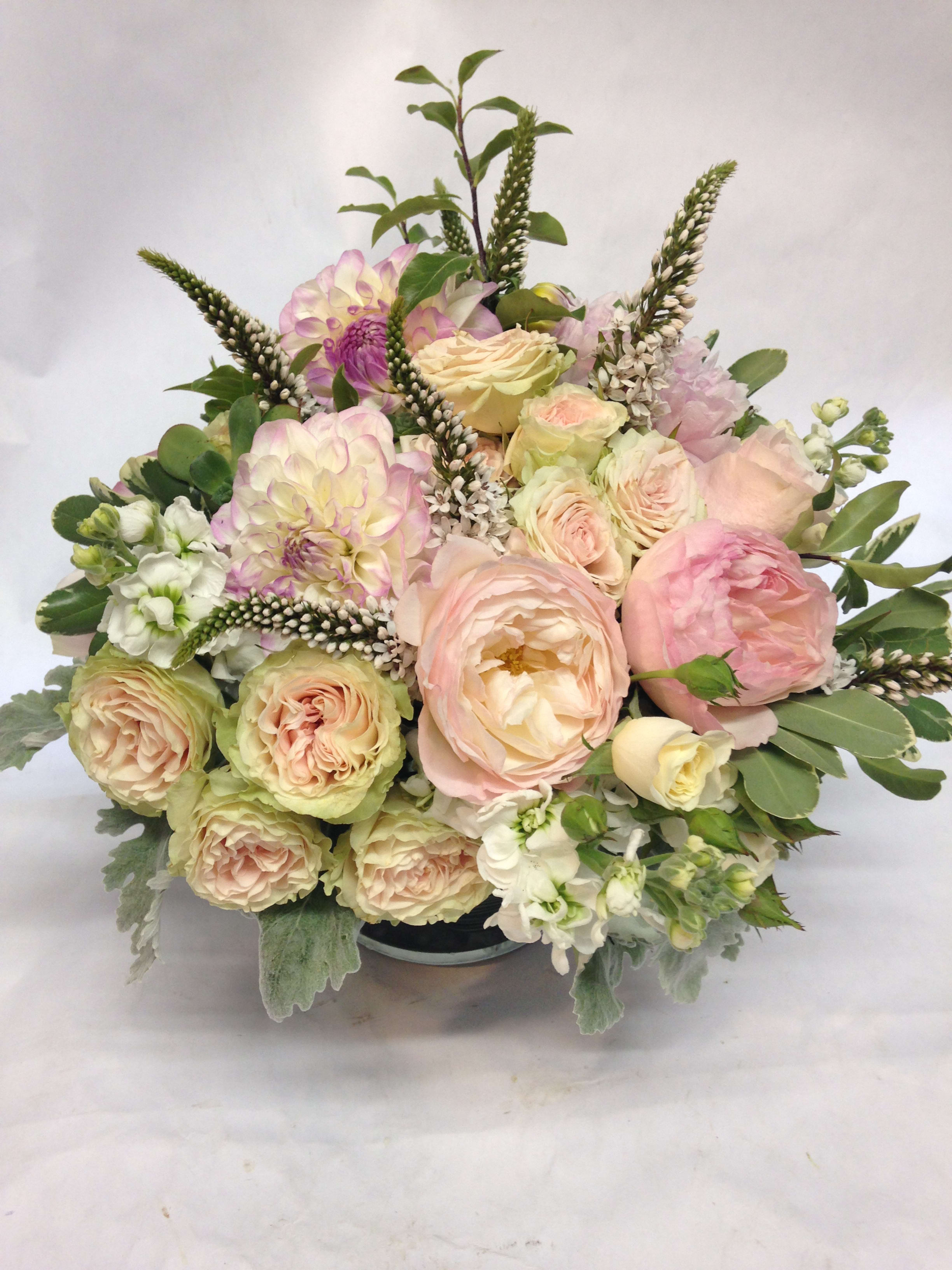 Pastel bouquet of roses, dahlias, and white flowers in a low container