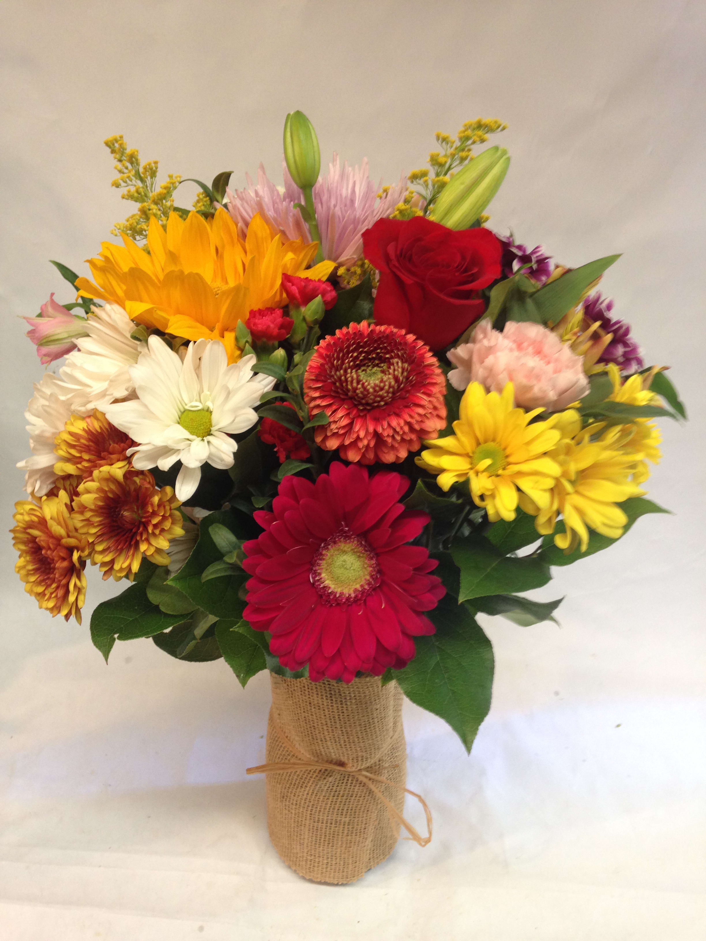 Mixed bouquet with sunflowers, roses, and daisies in a burlap-wrapped vase
